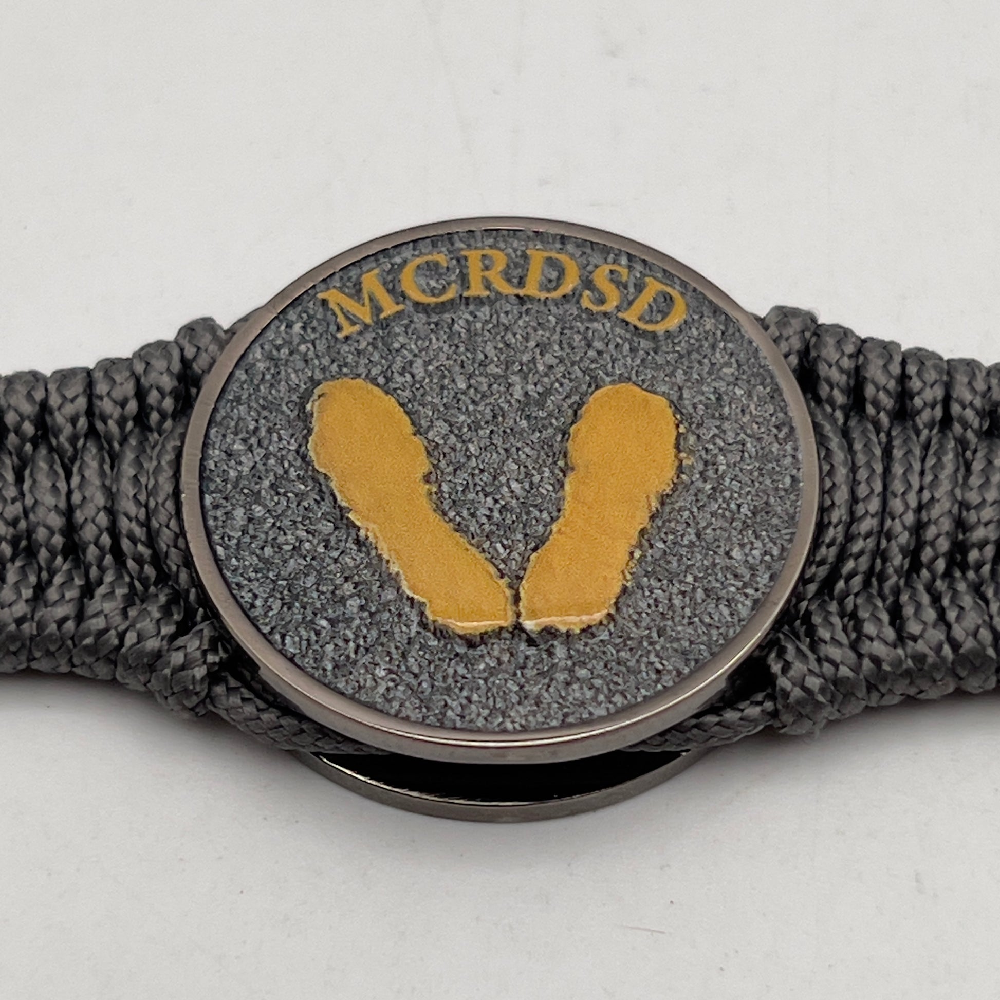 Thin, narrow, flexible and comfortable braided United States Marine Corps Recruit Depot Yellow Footprints bracelet featuring a black nickel plated UV enamel painted medallion replica of an actual set of USMC footprints, a silver Cobra style tactical buckle and woven with Charcoal Gray Type-1 paracord.