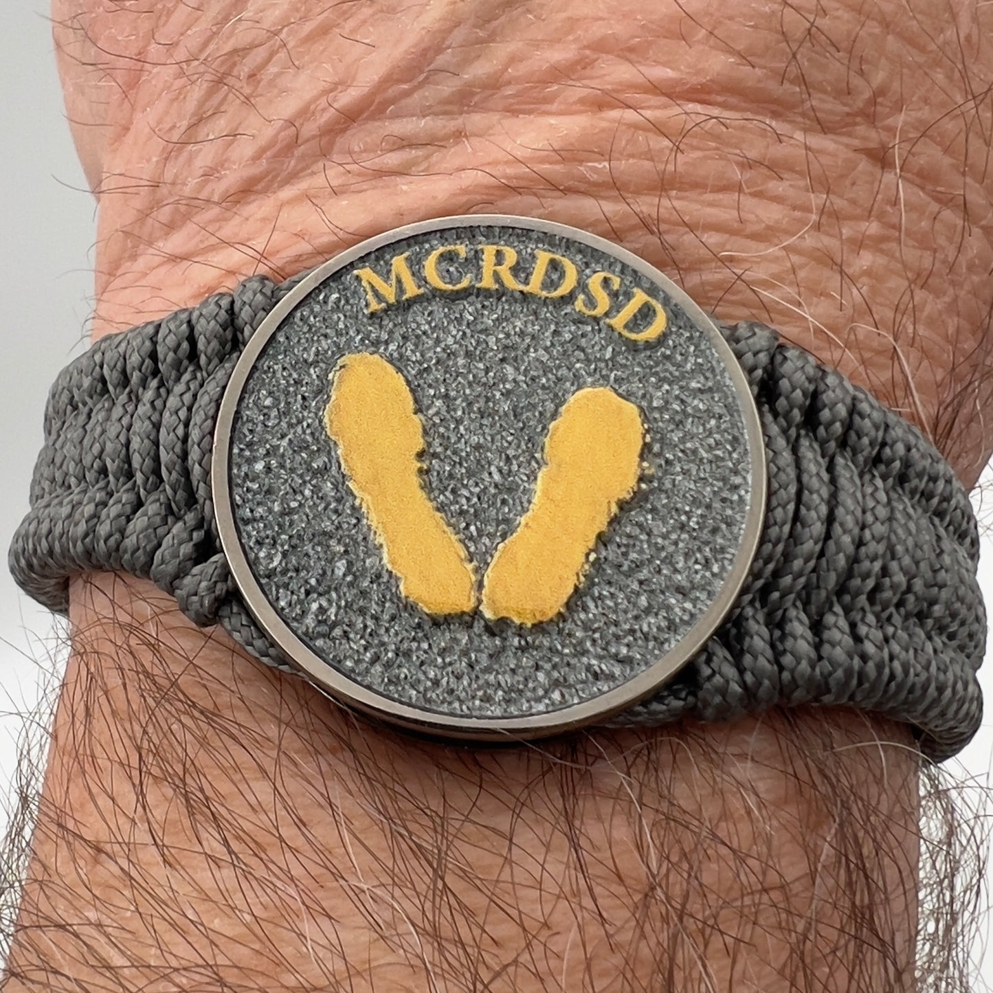Thin, narrow, flexible and comfortable braided United States Marine Corps Recruit Depot Yellow Footprints bracelet featuring a black nickel plated UV enamel painted medallion replica of an actual set of USMC footprints, a silver Cobra style tactical buckle and woven with Charcoal Gray Type-1 paracord.