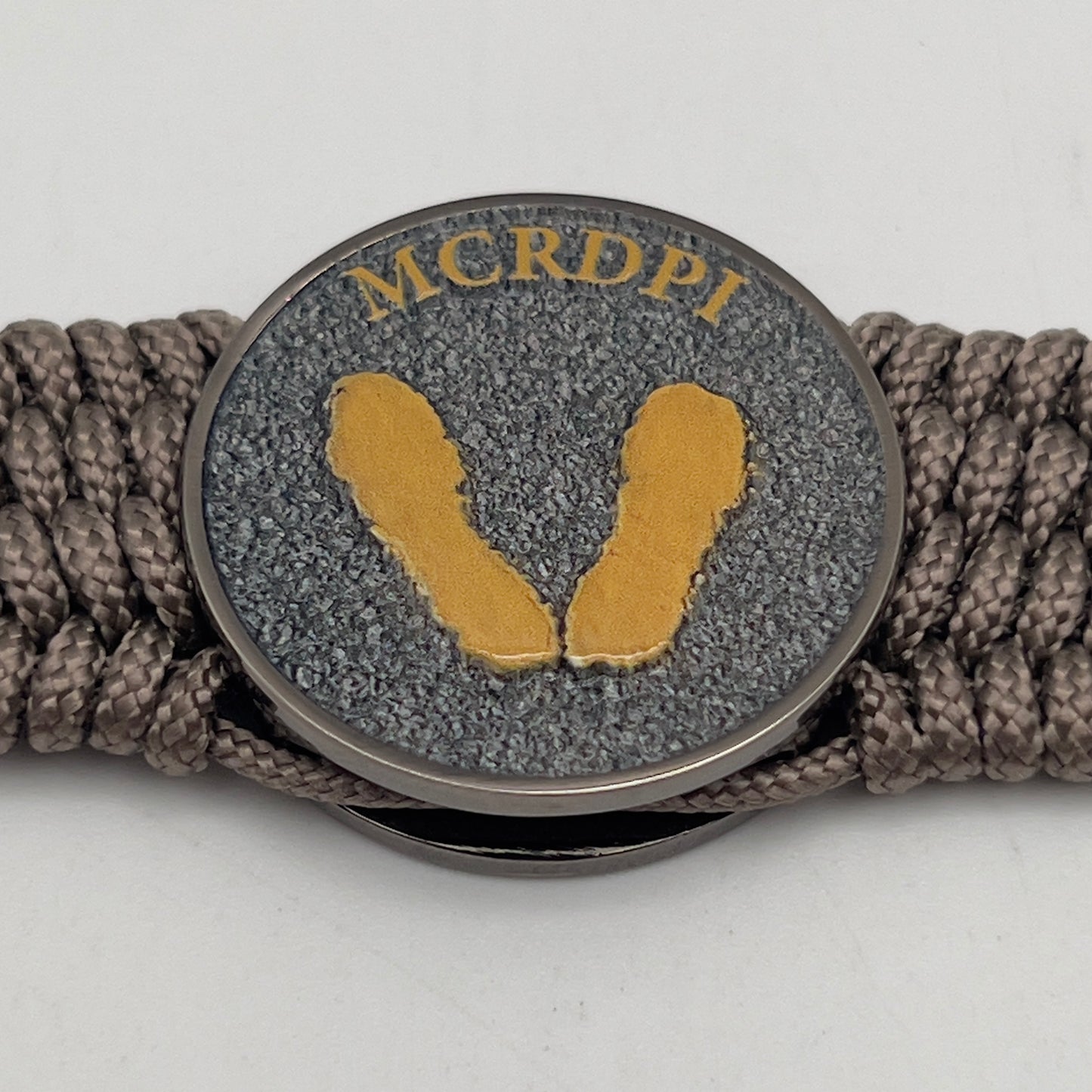 Thin, wide, flexible and comfortable braided United States Marine Corps Recruit Depot Yellow Footprints bracelet featuring a black nickel plated UV enamel painted medallion replica of an actual set of USMC recruit depot footprints, a gold Cobra style tactical buckle and woven with tan Type-1 paracord.