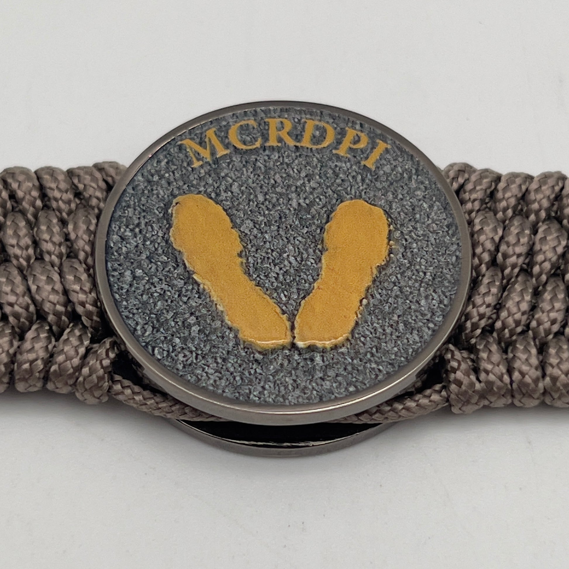 Thin, wide, flexible and comfortable braided United States Marine Corps Recruit Depot Yellow Footprints bracelet featuring a black nickel plated UV enamel painted medallion replica of an actual set of USMC recruit depot footprints, a gold Cobra style tactical buckle and woven with tan Type-1 paracord.