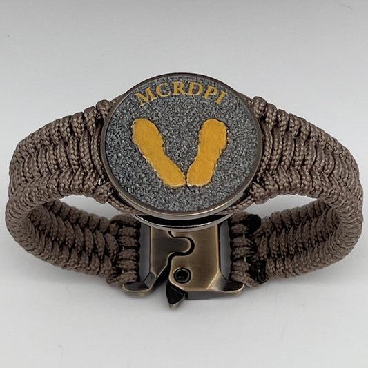 Thin, narrow, flexible and comfortable braided United States Marine Corps Recruit Depot Yellow Footprints bracelet featuring a black nickel plated UV enamel painted medallion replica of an actual set of USMC Yellow Footprints footprints, a gold Cobra style tactical buckle and woven with tan Type-1 paracord.