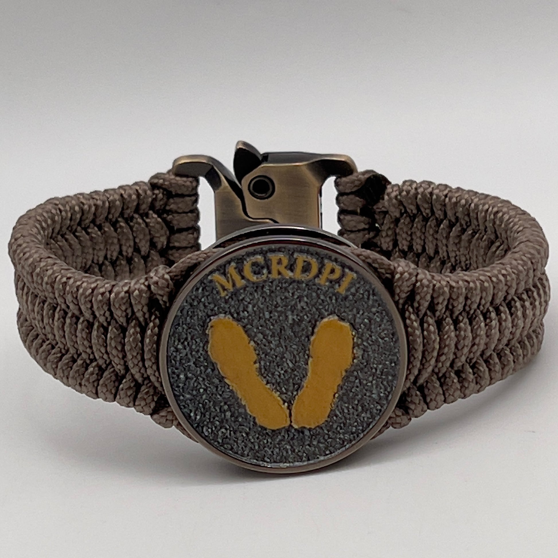 Thin, narrow, flexible and comfortable braided United States Marine Corps Recruit Depot Yellow Footprints bracelet featuring a black nickel plated UV enamel painted medallion replica of an actual set of USMC Yellow Footprints footprints, a gold Cobra style tactical buckle and woven with tan Type-1 paracord.