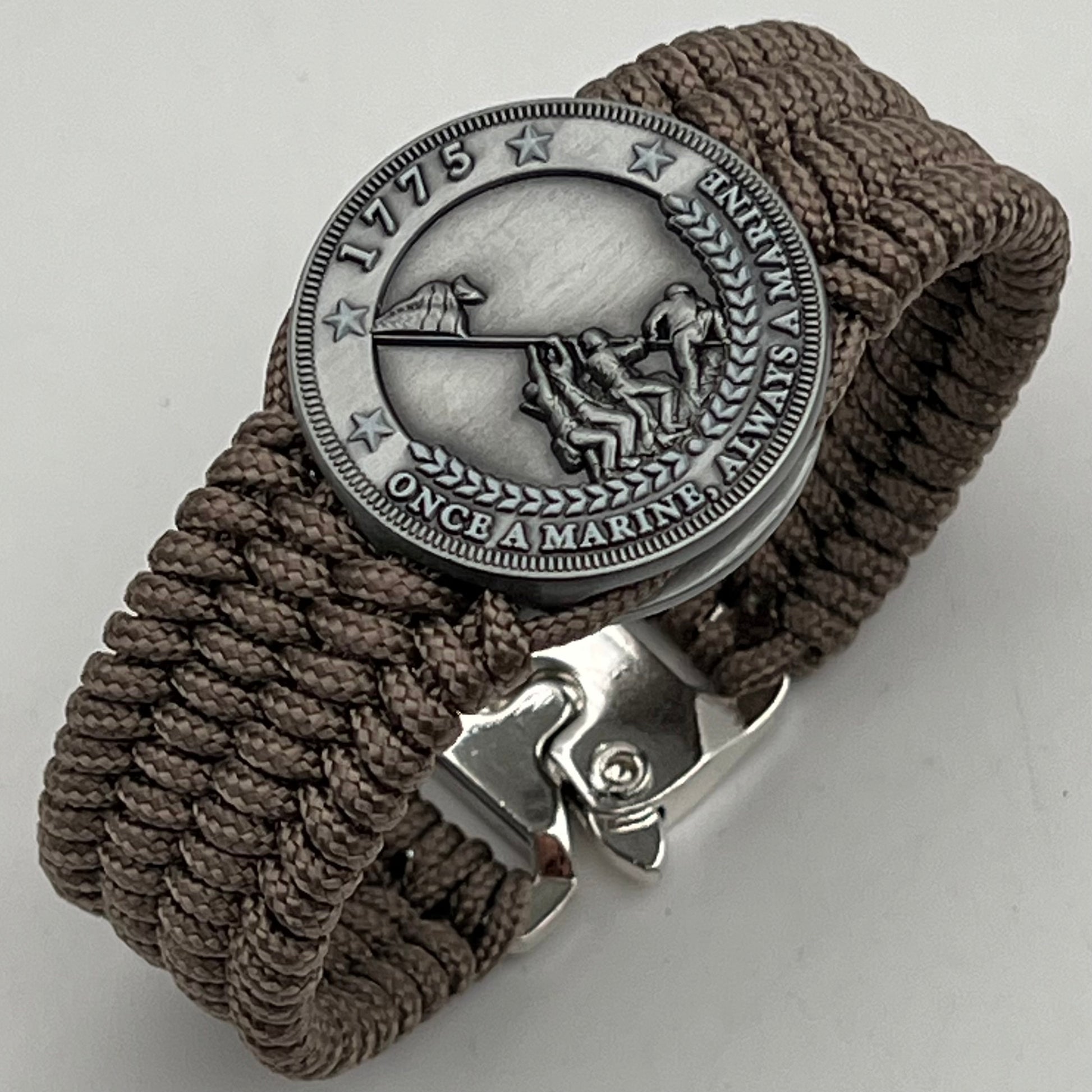 Thin, wide, flexible and comfortable braided United States Marine Corps Iwo Jima bracelet featuring an antique silver plated Iwo Jima flag raising medallion, a silver Cobra style tactical buckle and woven with tan type-1 paracord.