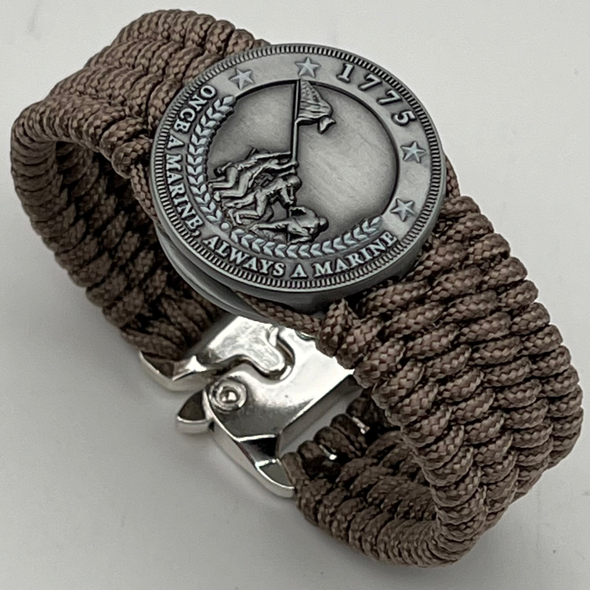 Thin, wide, flexible and comfortable braided United States Marine Corps Iwo Jima bracelet featuring an antique silver plated Iwo Jima flag raising medallion, a silver Cobra style tactical buckle and woven with tan type-1 paracord.