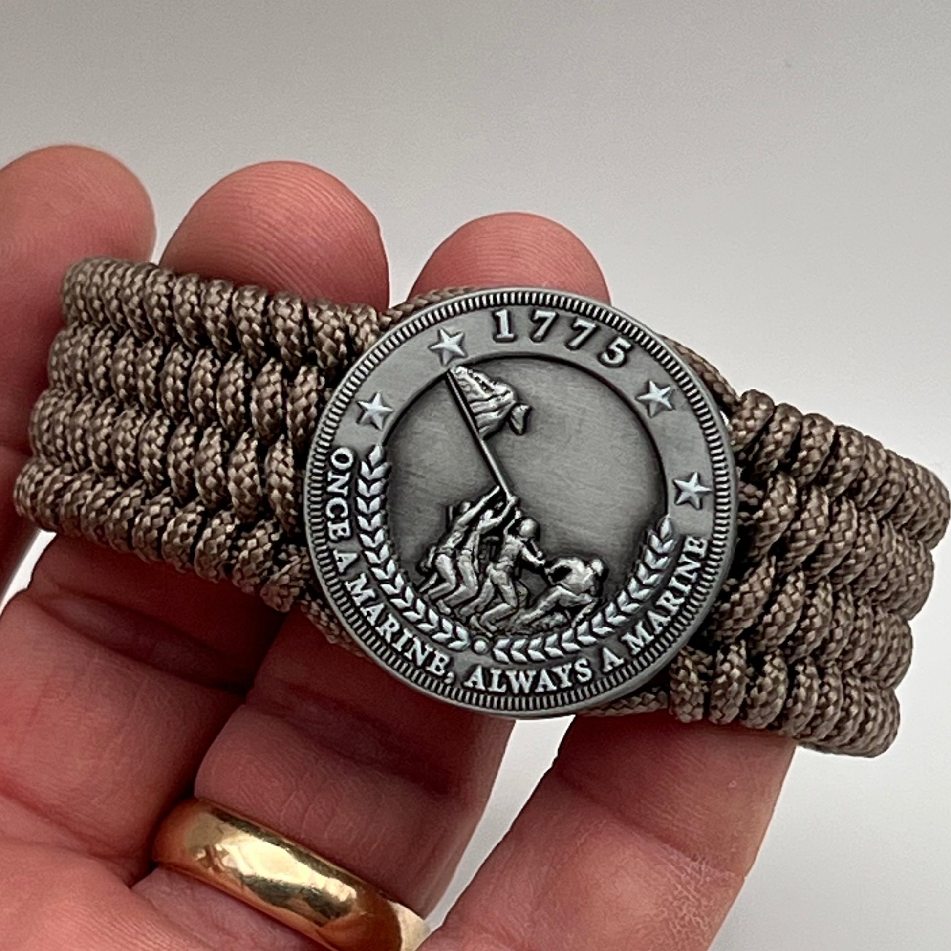 Thin, wide, flexible and comfortable braided United States Marine Corps Iwo Jima bracelet featuring an antique silver plated Iwo Jima flag raising medallion, a silver Cobra style tactical buckle and woven with tan type-1 paracord.