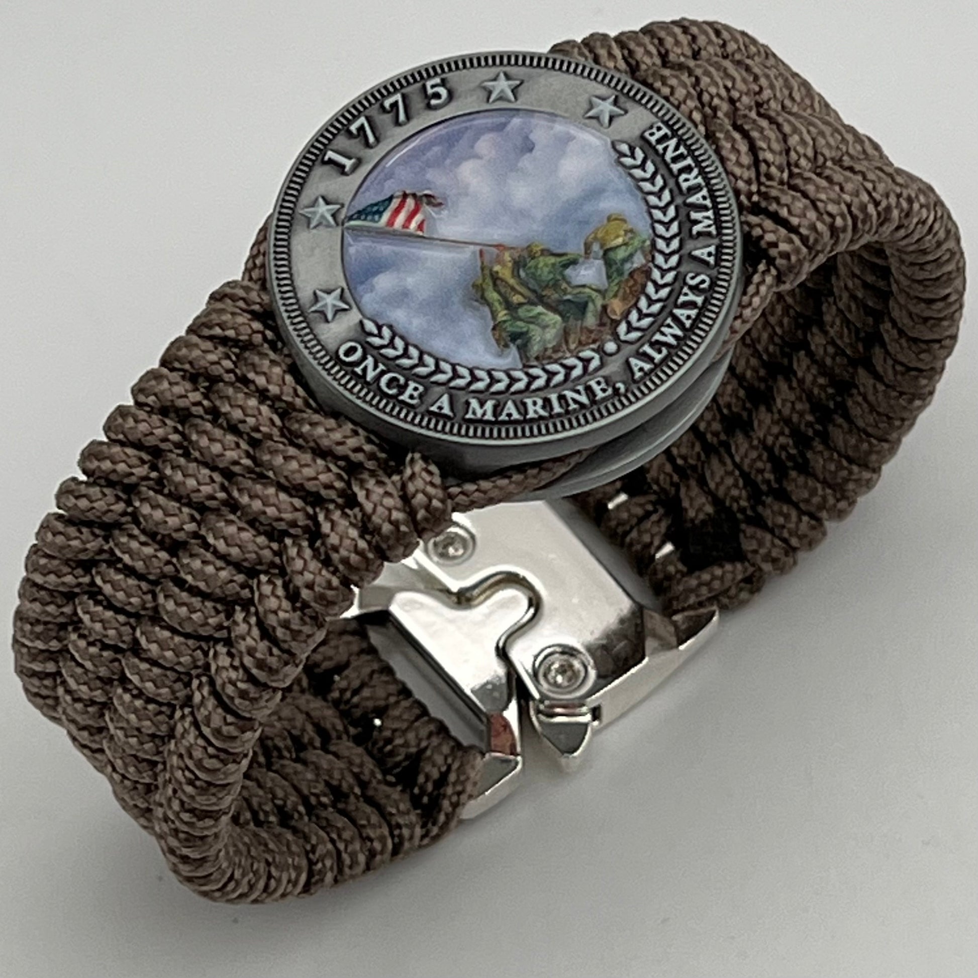 Thin, wide, flexible and comfortable braided United States Marine Corps Iwo Jima bracelet featuring an antique silver plated UV painted Iwo Jima flag raising medallion, a silver Cobra style tactical buckle and woven with tan Type-1 paracord.
