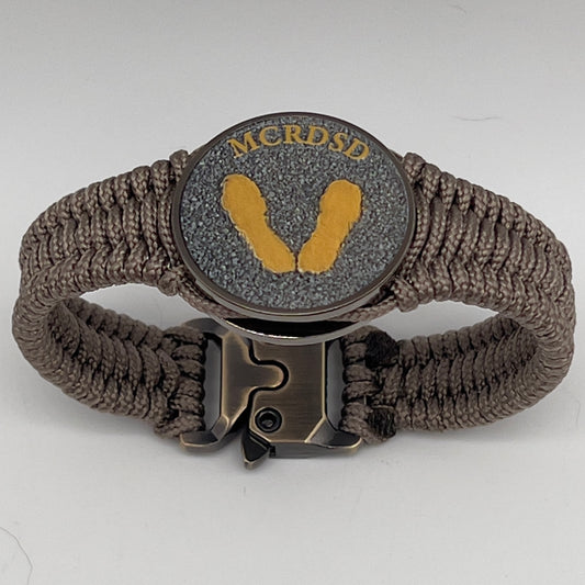 Thin, narrow, flexible and comfortable braided United States Marine Corps Recruit Depot Yellow Footprints bracelet featuring a black nickel plated UV enamel painted medallion replica of an actual set of USMC recruit depot footprints, a gold Cobra style tactical buckle and woven with tan Type-1 paracord.