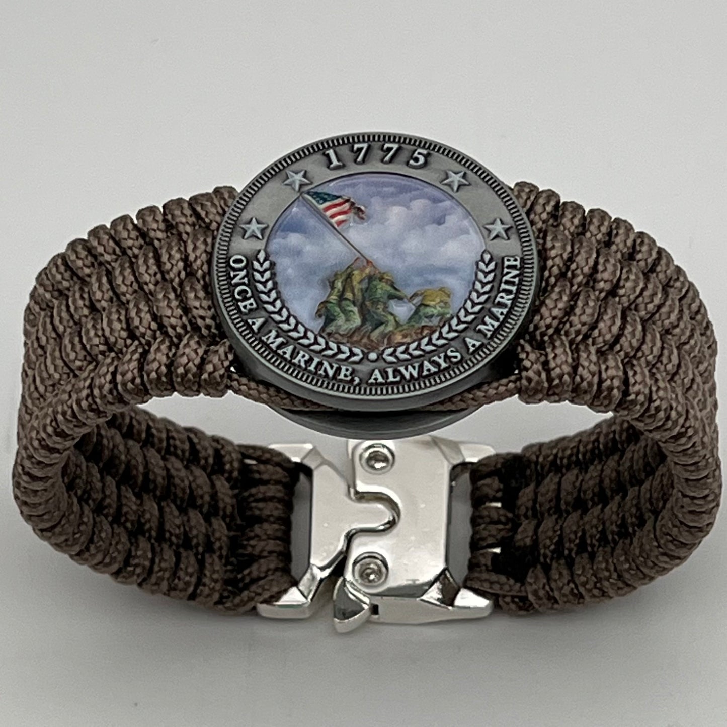 Thin, wide, flexible and comfortable braided United States Marine Corps Iwo Jima bracelet featuring an antique silver plated UV painted Iwo Jima flag raising medallion, a silver Cobra style tactical buckle and woven with tan Type-1 paracord.