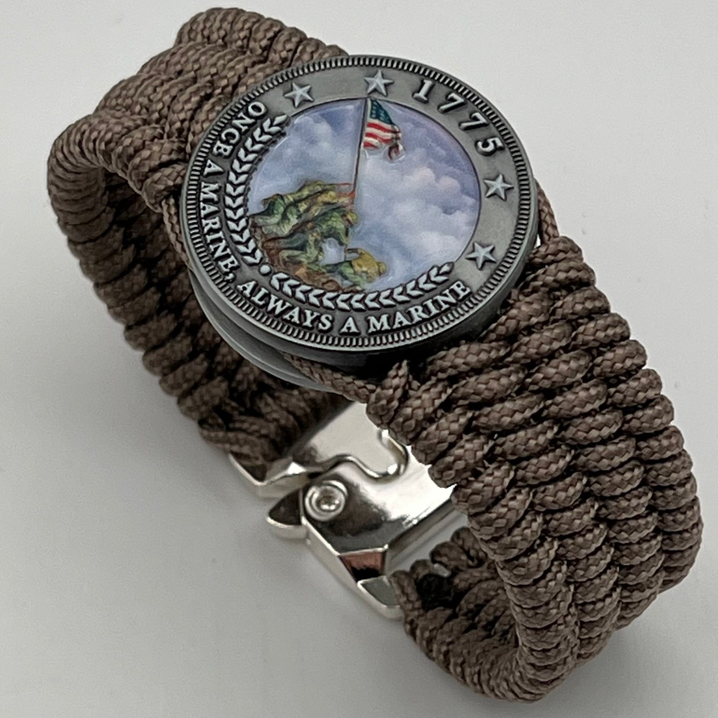 Thin, wide, flexible and comfortable braided United States Marine Corps Iwo Jima bracelet featuring an antique silver plated UV painted Iwo Jima flag raising medallion, a silver Cobra style tactical buckle and woven with tan Type-1 paracord.