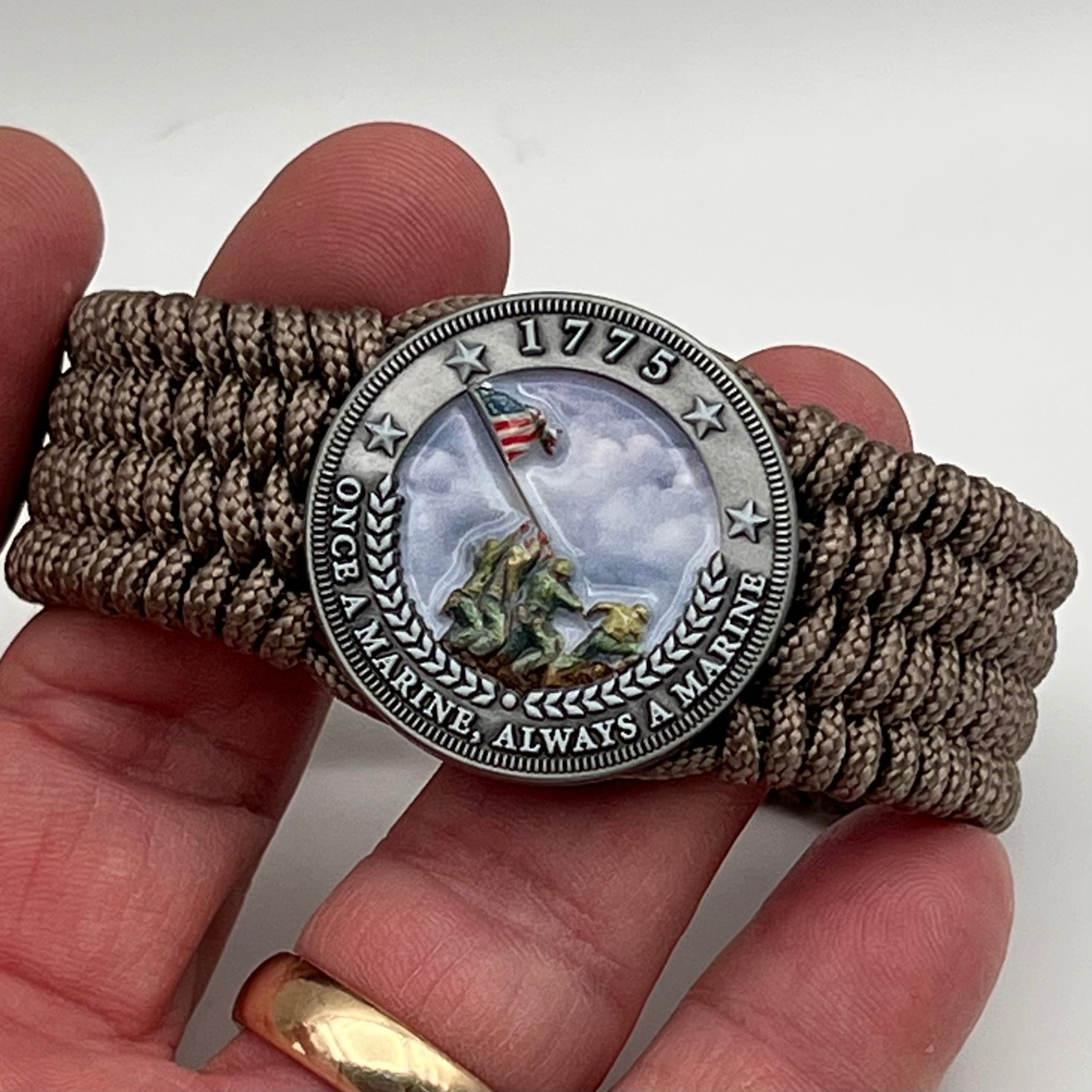 Thin, wide, flexible and comfortable braided United States Marine Corps Iwo Jima bracelet featuring an antique silver plated UV painted Iwo Jima flag raising medallion, a silver Cobra style tactical buckle and woven with tan Type-1 paracord.