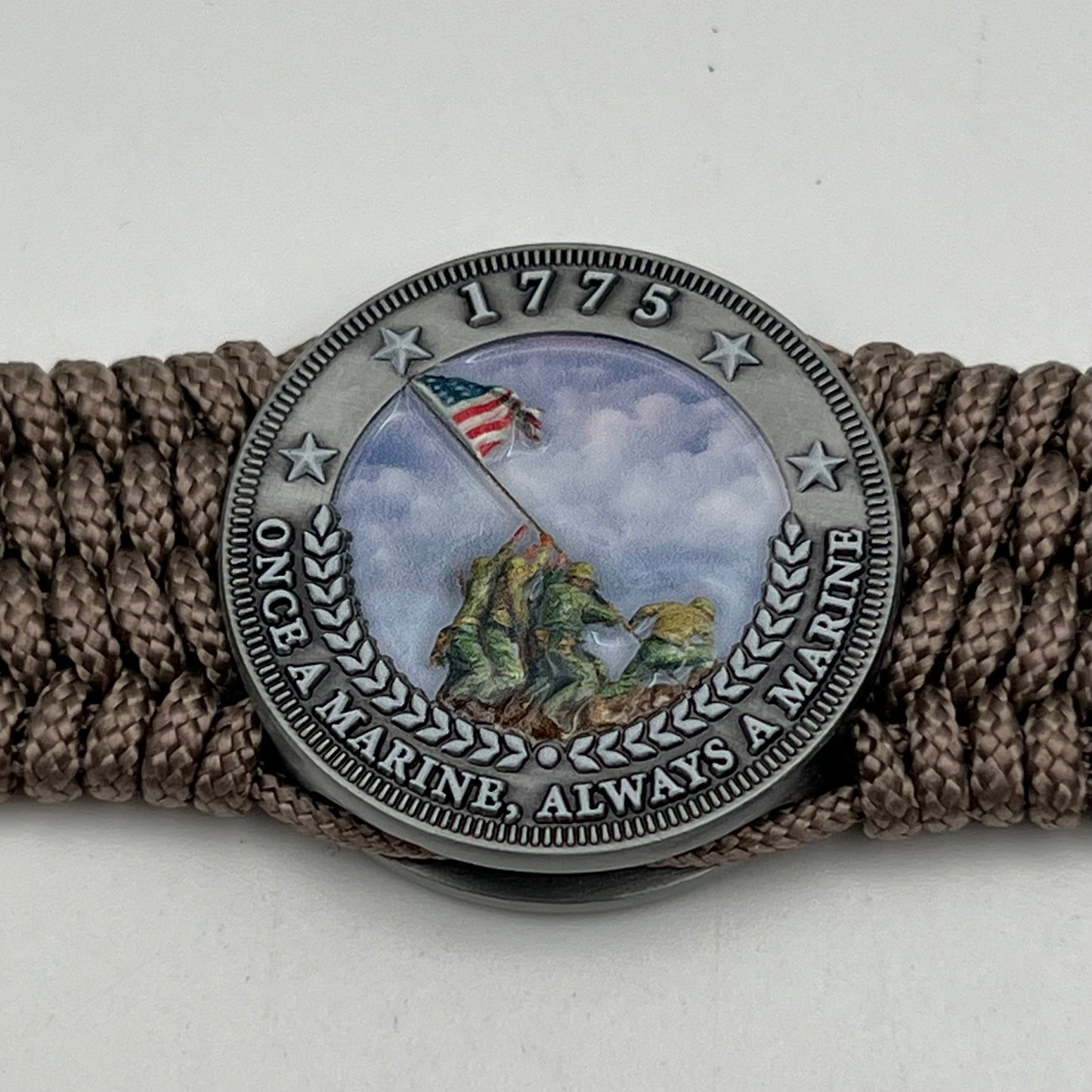 Thin, wide, flexible and comfortable braided United States Marine Corps Iwo Jima bracelet featuring an antique silver plated UV painted Iwo Jima flag raising medallion, a silver Cobra style tactical buckle and woven with tan Type-1 paracord.