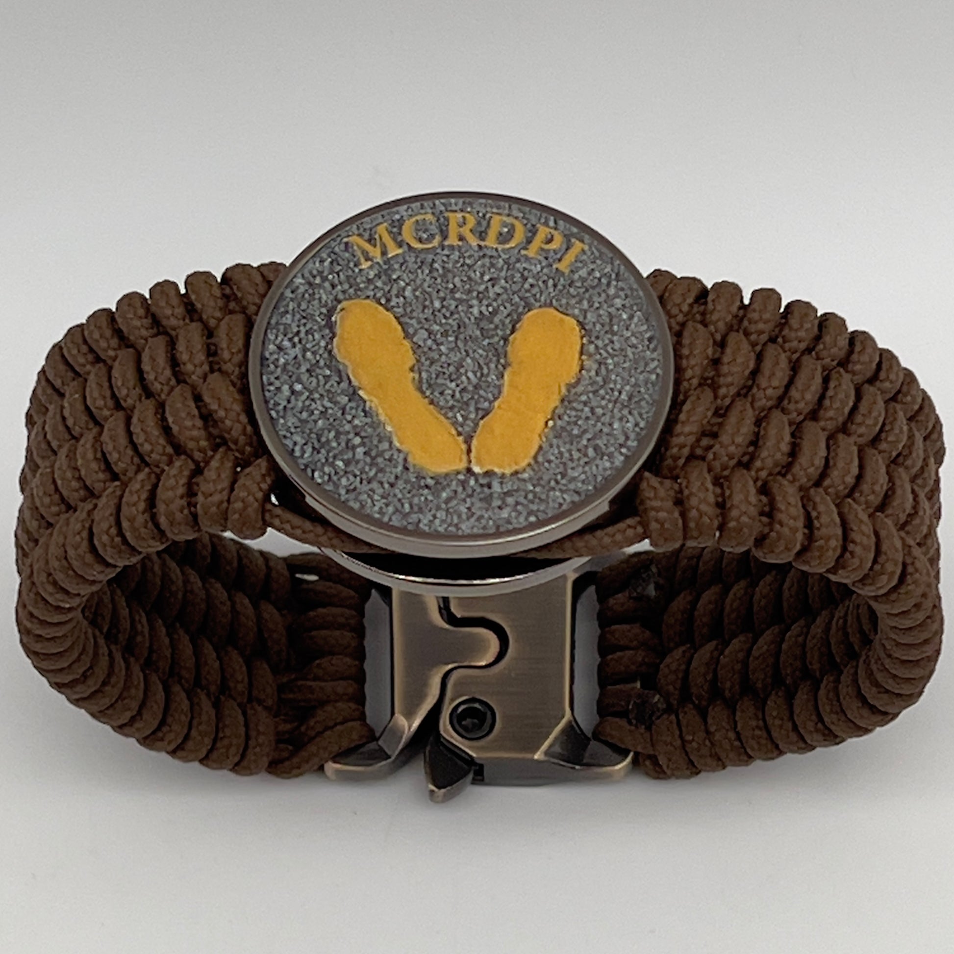 Thin, wide, flexible and comfortable braided United States Marine Corps Recruit Depot Yellow Footprints bracelet featuring a black nickel plated UV enamel painted medallion replica of an actual set of USMC footprints, a gold Cobra style tactical buckle and woven with Coyote Brown Type-1 paracord.