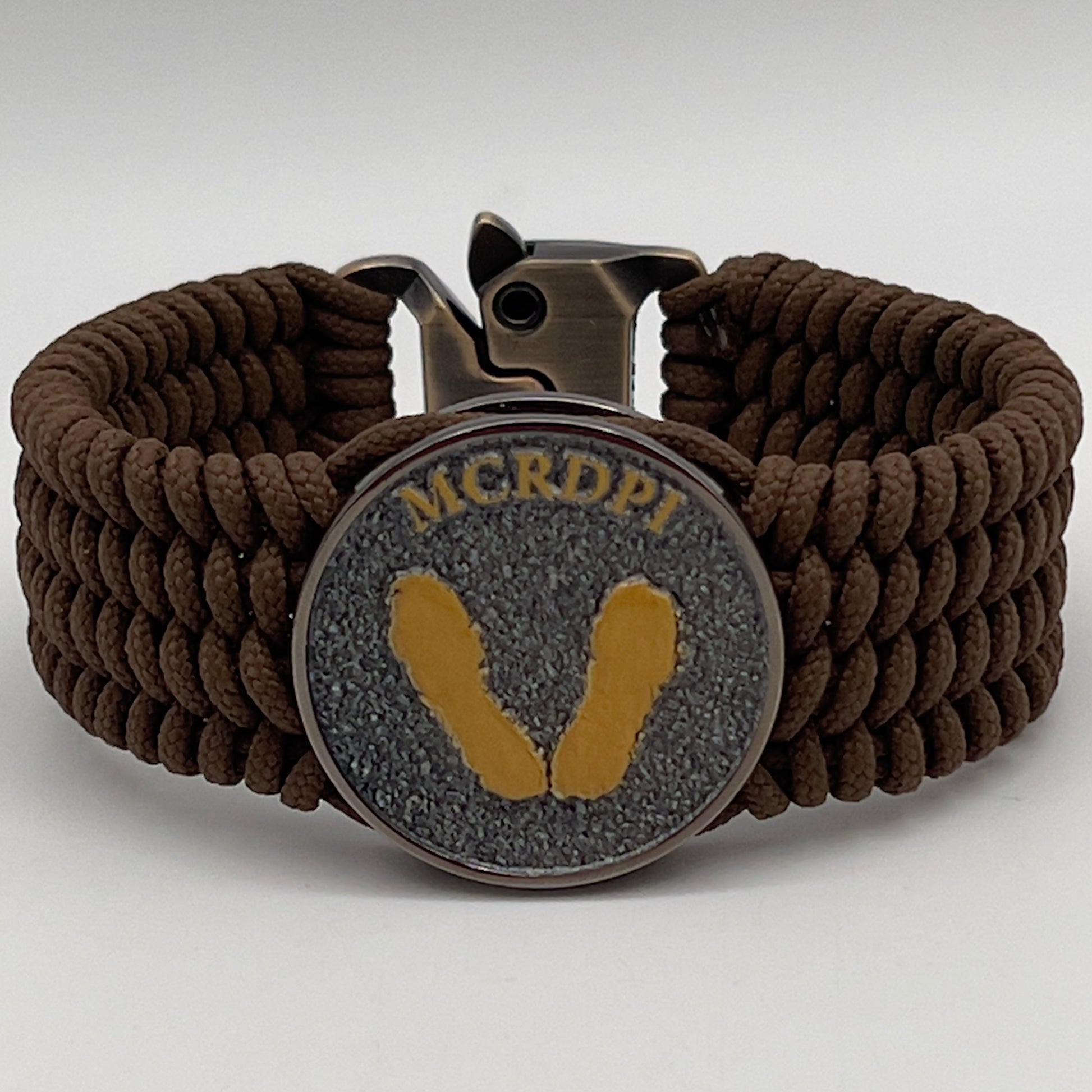 Thin, wide, flexible and comfortable braided United States Marine Corps Recruit Depot Yellow Footprints bracelet featuring a black nickel plated UV enamel painted medallion replica of an actual set of USMC footprints, a gold Cobra style tactical buckle and woven with Coyote Brown Type-1 paracord.