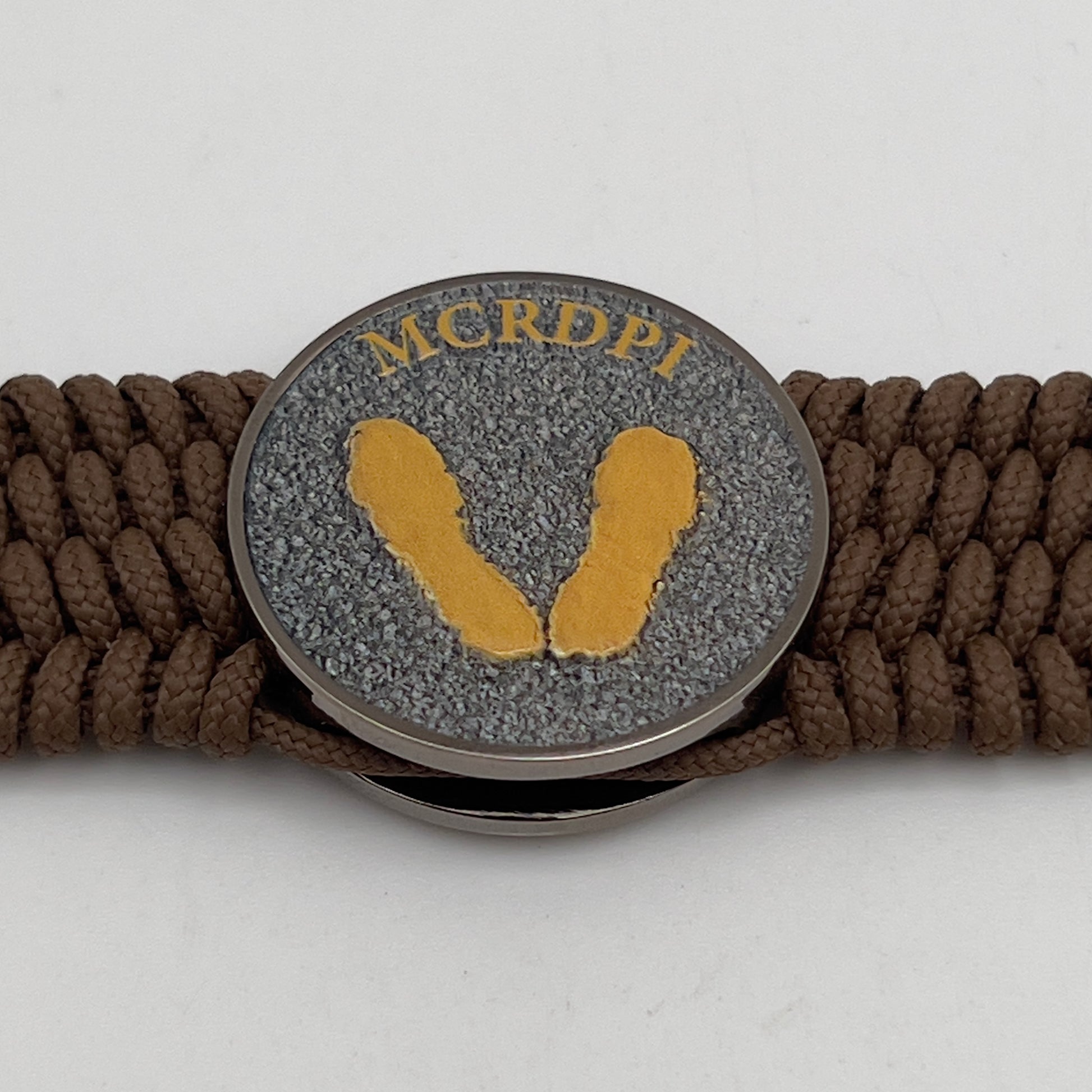 Thin, wide, flexible and comfortable braided United States Marine Corps Recruit Depot Yellow Footprints bracelet featuring a black nickel plated UV enamel painted medallion replica of an actual set of USMC footprints, a gold Cobra style tactical buckle and woven with Coyote Brown Type-1 paracord.