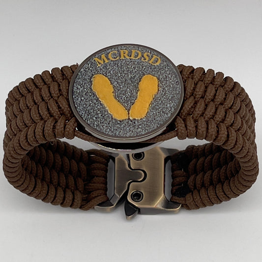 Thin, wide, flexible and comfortable braided United States Marine Corps Recruit Depot Yellow Footprints bracelet featuring a black nickel plated UV enamel painted medallion replica of an actual set of USMC footprints, a gold Cobra style tactical buckle and woven with Coyote Brown Type-1 paracord.