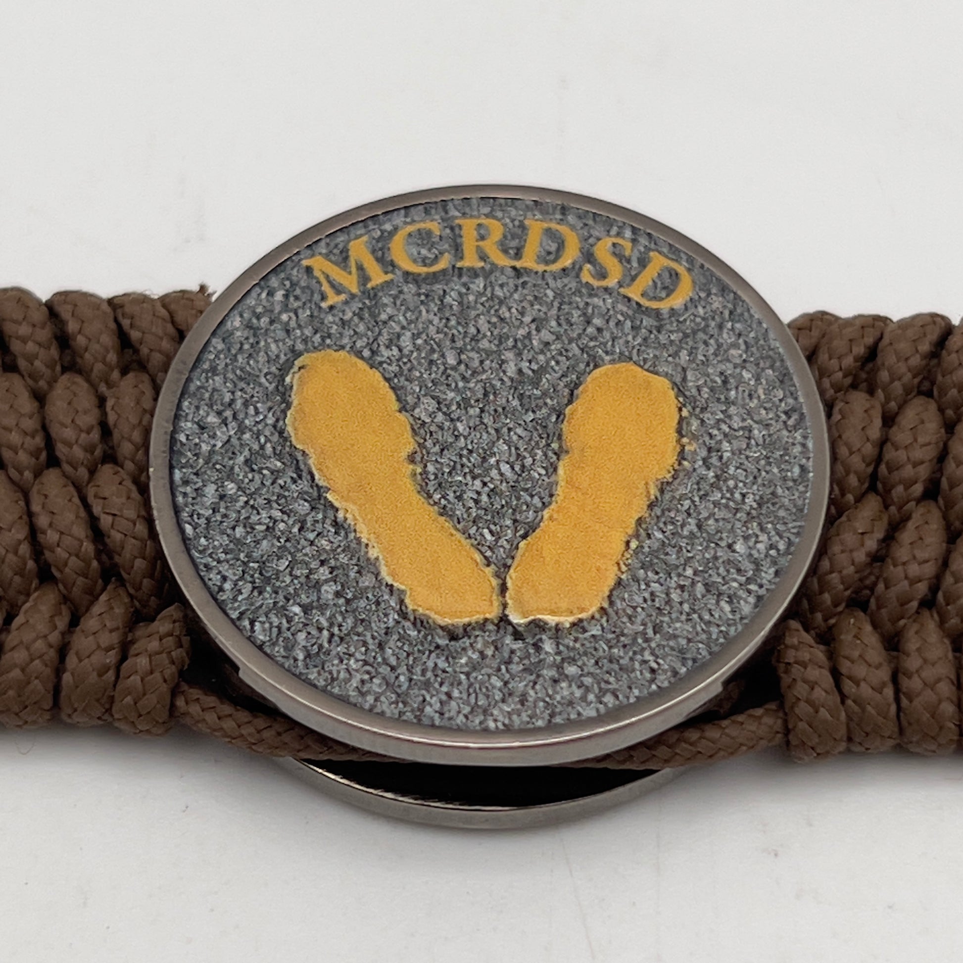 Thin, wide, flexible and comfortable braided United States Marine Corps Recruit Depot Yellow Footprints bracelet featuring a black nickel plated UV enamel painted medallion replica of an actual set of USMC footprints, a gold Cobra style tactical buckle and woven with Coyote Brown Type-1 paracord.