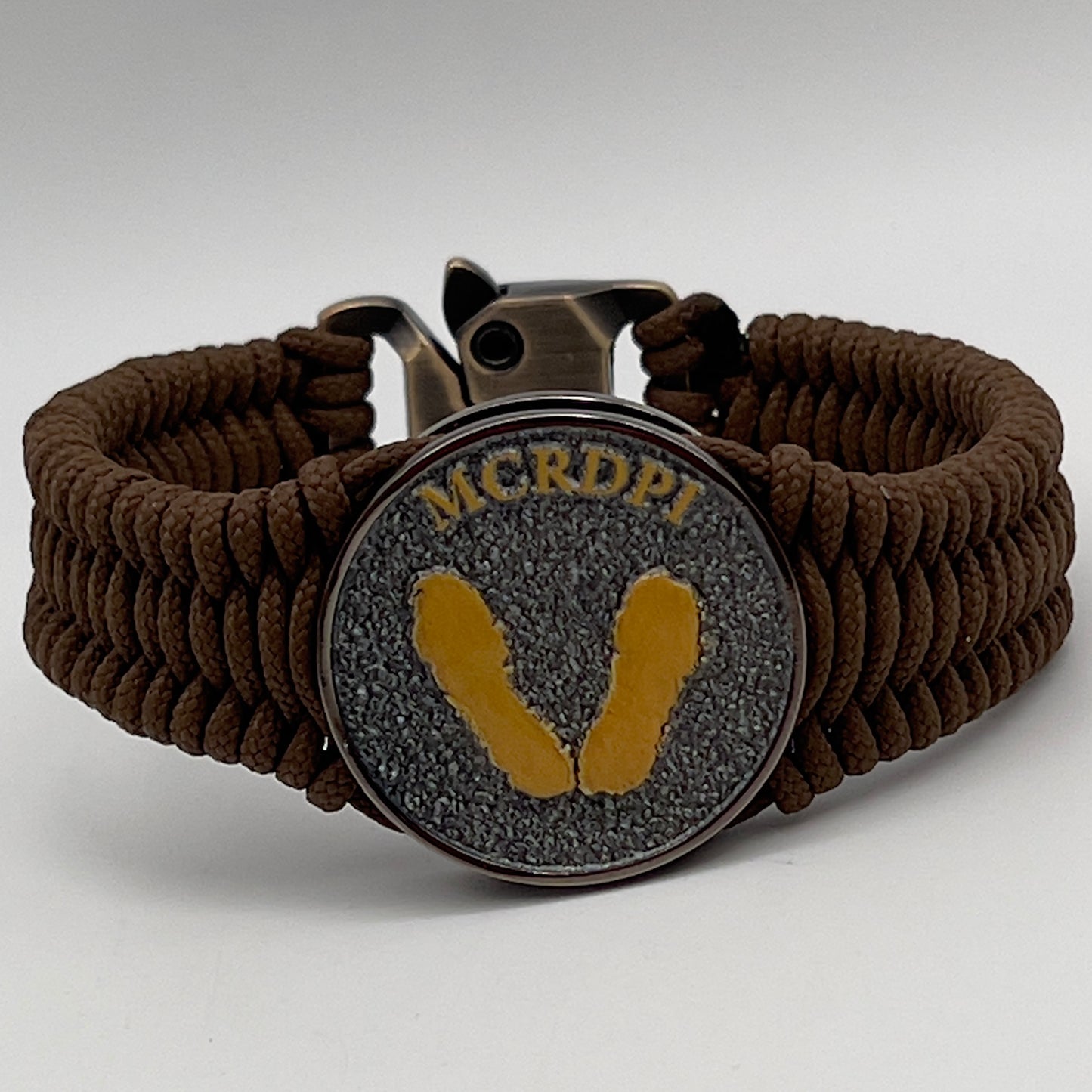 Thin, narrow, flexible and comfortable braided United States Marine Corps Recruit Depot Yellow Footprints bracelet featuring a black nickel plated UV enamel painted medallion replica of an actual set of USMC recruit depot footprints, a gold Cobra style tactical buckle and woven with Coyote Brown type-1 paracord.