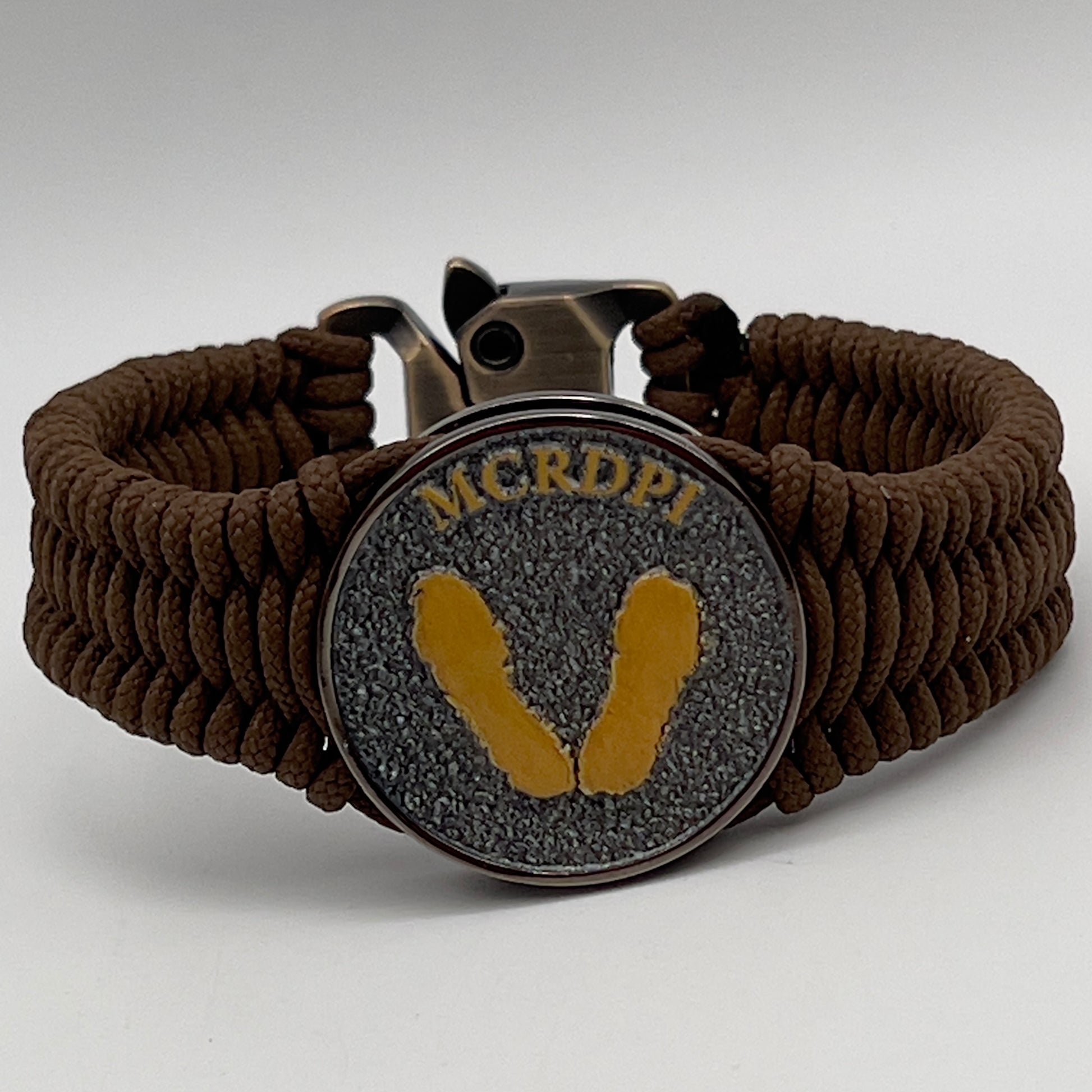 Thin, narrow, flexible and comfortable braided United States Marine Corps Recruit Depot Yellow Footprints bracelet featuring a black nickel plated UV enamel painted medallion replica of an actual set of USMC recruit depot footprints, a gold Cobra style tactical buckle and woven with Coyote Brown type-1 paracord.