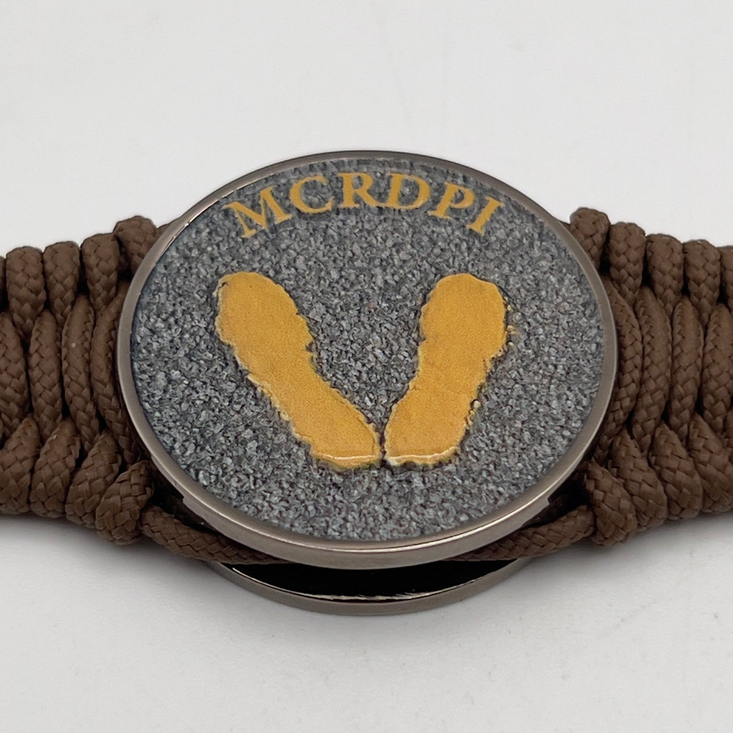 Thin, narrow, flexible and comfortable braided United States Marine Corps Recruit Depot Yellow Footprints bracelet featuring a black nickel plated UV enamel painted medallion replica of an actual set of USMC recruit depot footprints, a gold Cobra style tactical buckle and woven with Coyote Brown type-1 paracord.