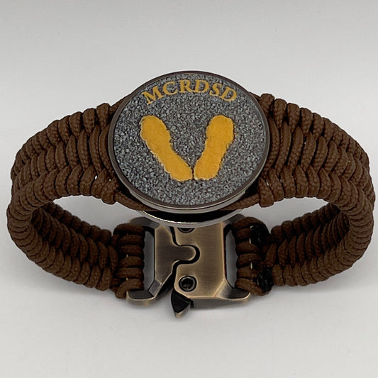 Thin, narrow, flexible and comfortable braided United States Marine Corps Recruit Depot Yellow Footprints bracelet featuring a black nickel plated UV enamel painted medallion replica of an actual set of USMC recruit depot footprints, a gold Cobra style tactical buckle and woven with Coyote Brown type-1 paracord.