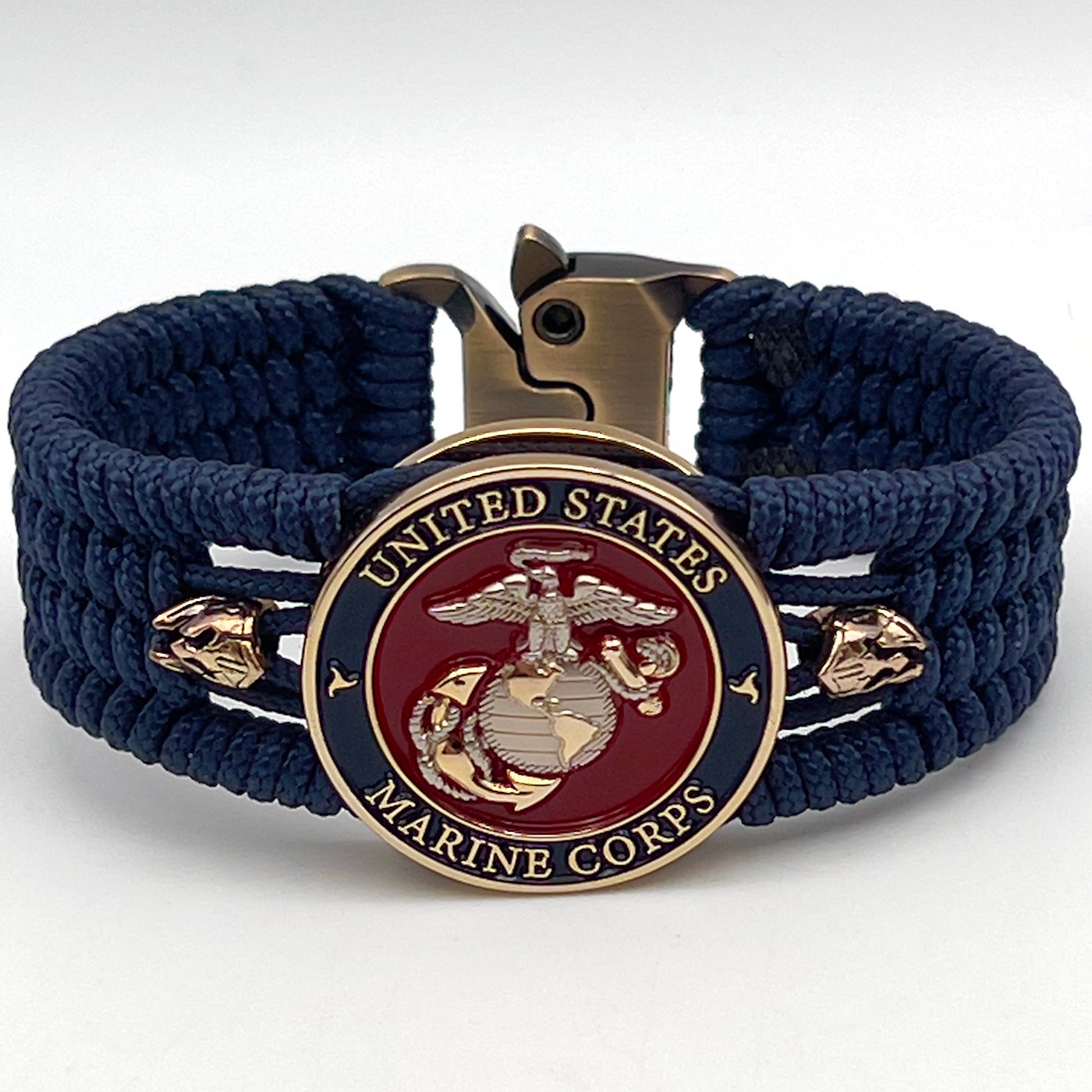 Thin, medium width, flexible and comfortable braided United States Marine Corps bracelet featuring a 24K gold and silver plated USMC officer Eagle Globe and Anchor medallion, two brass Spartan helmets, a gold Cobra style tactical buckle and woven with Navy Blue type-1 paracord.
