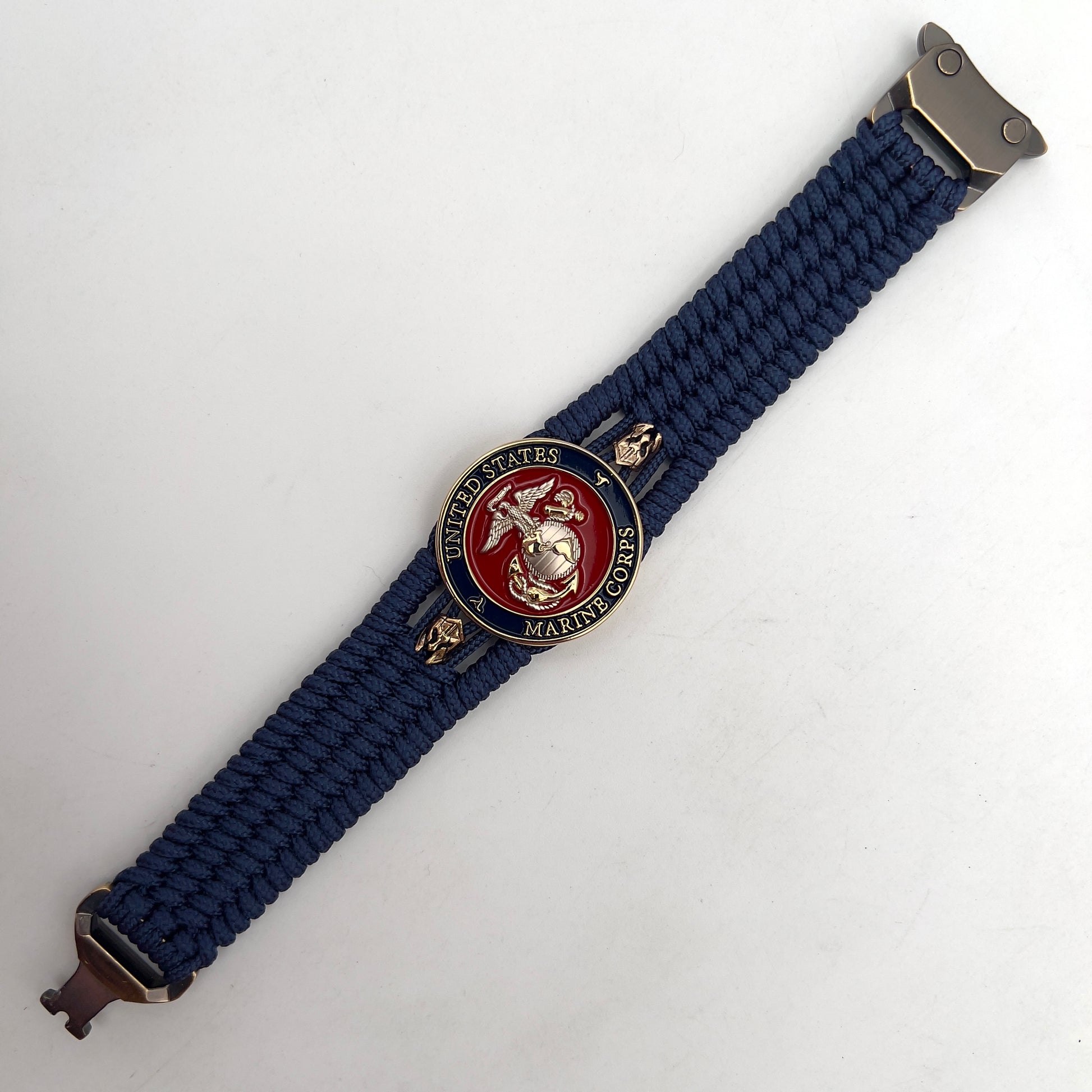 Thin, medium width, flexible and comfortable braided United States Marine Corps bracelet featuring a 24K gold and silver plated USMC officer Eagle Globe and Anchor medallion, two brass Spartan helmets, a gold Cobra style tactical buckle and woven with Navy Blue type-1 paracord.