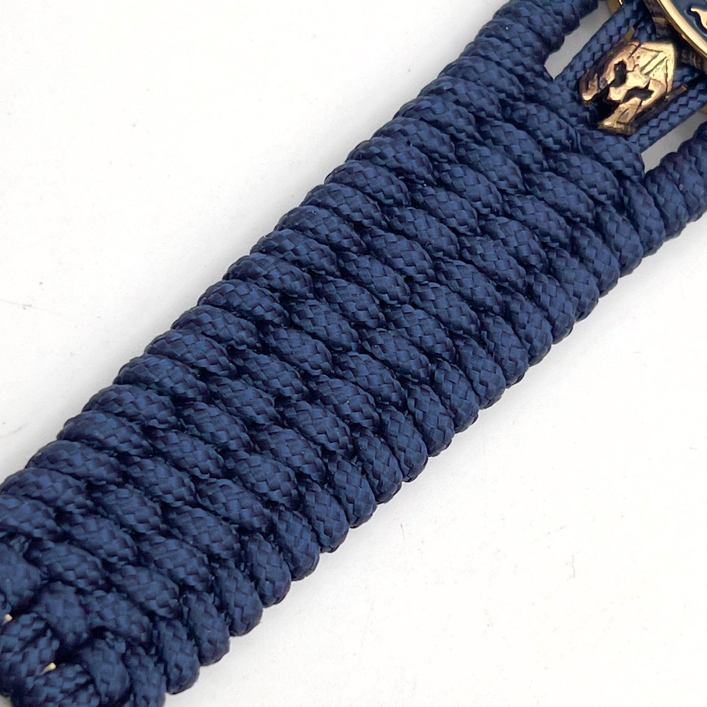 Thin, medium width, flexible and comfortable braided United States Marine Corps bracelet featuring a 24K gold and silver plated USMC officer Eagle Globe and Anchor medallion, two brass Spartan helmets, a gold Cobra style tactical buckle and woven with Navy Blue type-1 paracord.