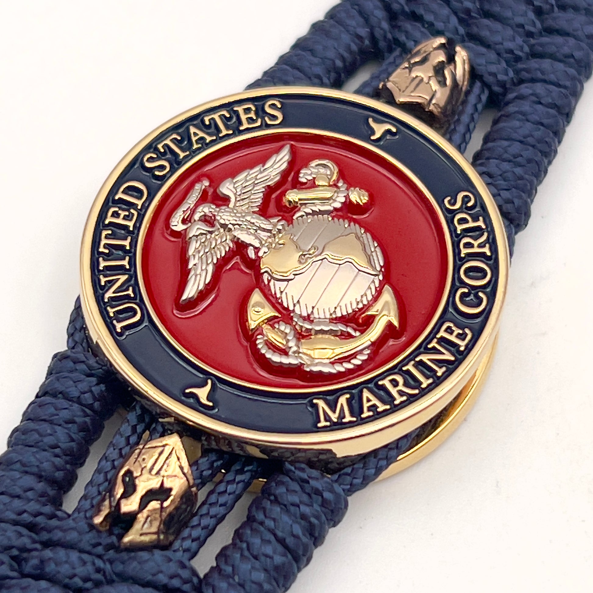 Thin, medium width, flexible and comfortable braided United States Marine Corps bracelet featuring a 24K gold and silver plated USMC officer Eagle Globe and Anchor medallion, two brass Spartan helmets, a gold Cobra style tactical buckle and woven with Navy Blue type-1 paracord.