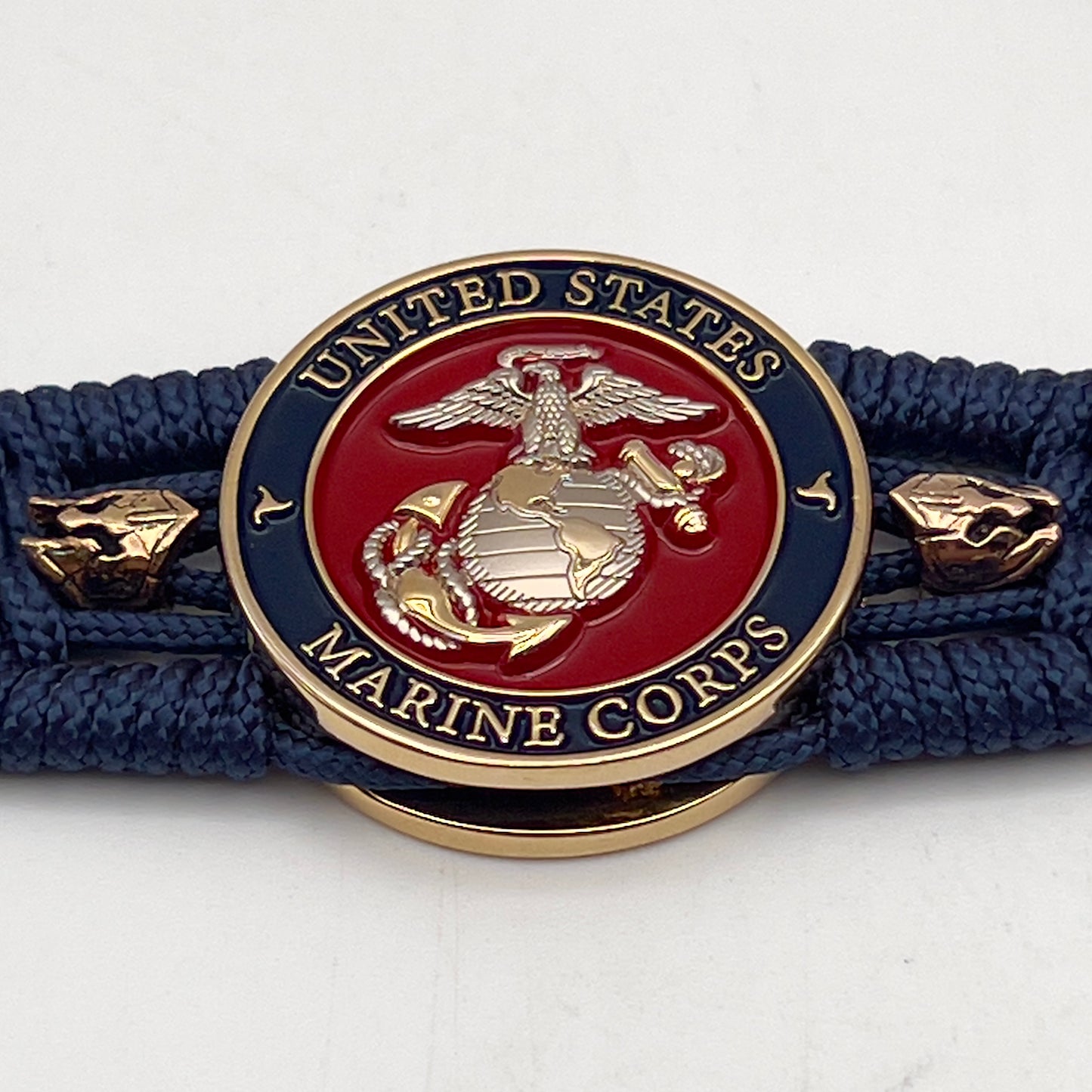 Thin, medium width, flexible and comfortable braided United States Marine Corps bracelet featuring a 24K gold and silver plated USMC officer Eagle Globe and Anchor medallion, two brass Spartan helmets, a gold Cobra style tactical buckle and woven with Navy Blue type-1 paracord.