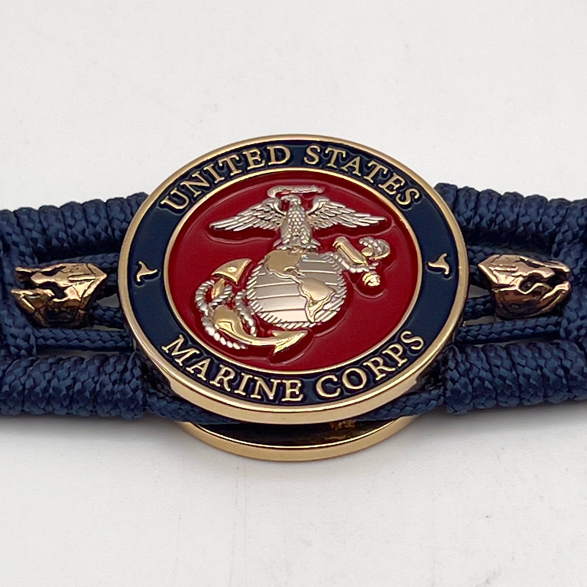 Thin, medium width, flexible and comfortable braided United States Marine Corps bracelet featuring a 24K gold and silver plated USMC officer Eagle Globe and Anchor medallion, two brass Spartan helmets, a gold Cobra style tactical buckle and woven with Navy Blue type-1 paracord.
