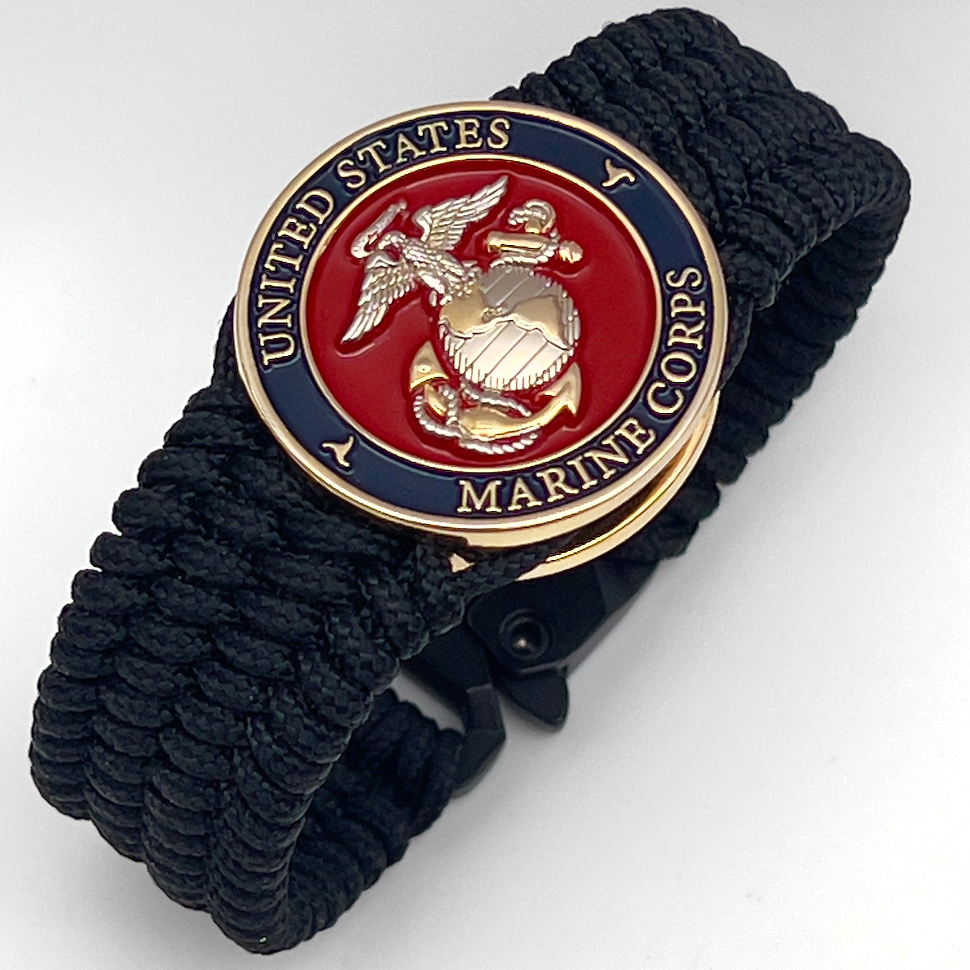 Thin, wide, flexible and comfortable braided United States Marine Corps bracelet featuring a 24K gold and silver plated USMC Eagle Globe and Anchor medallion, a black Cobra style tactical buckle and woven with black type-1 paracord.