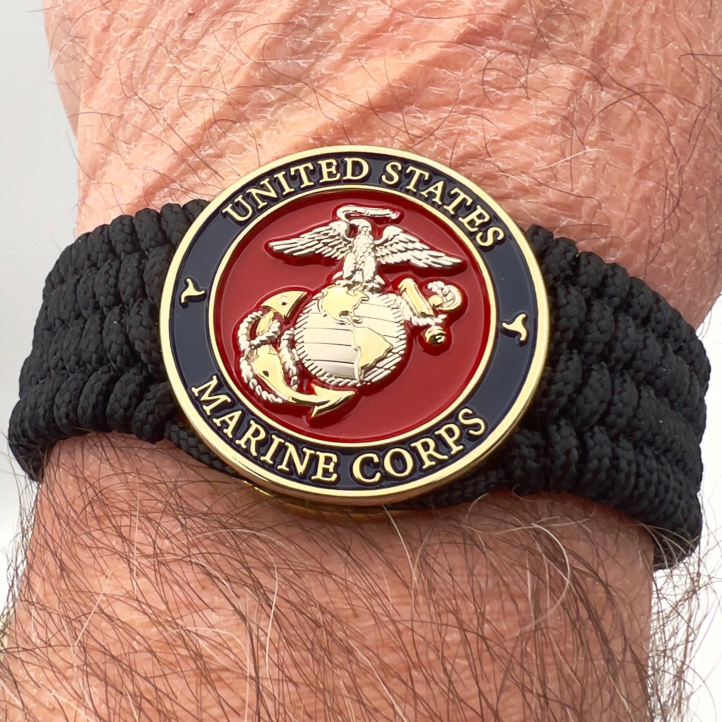 Thin, wide, flexible and comfortable braided United States Marine Corps bracelet featuring a 24K gold and silver plated USMC Eagle Globe and Anchor medallion, a black Cobra style tactical buckle and woven with black type-1 paracord.