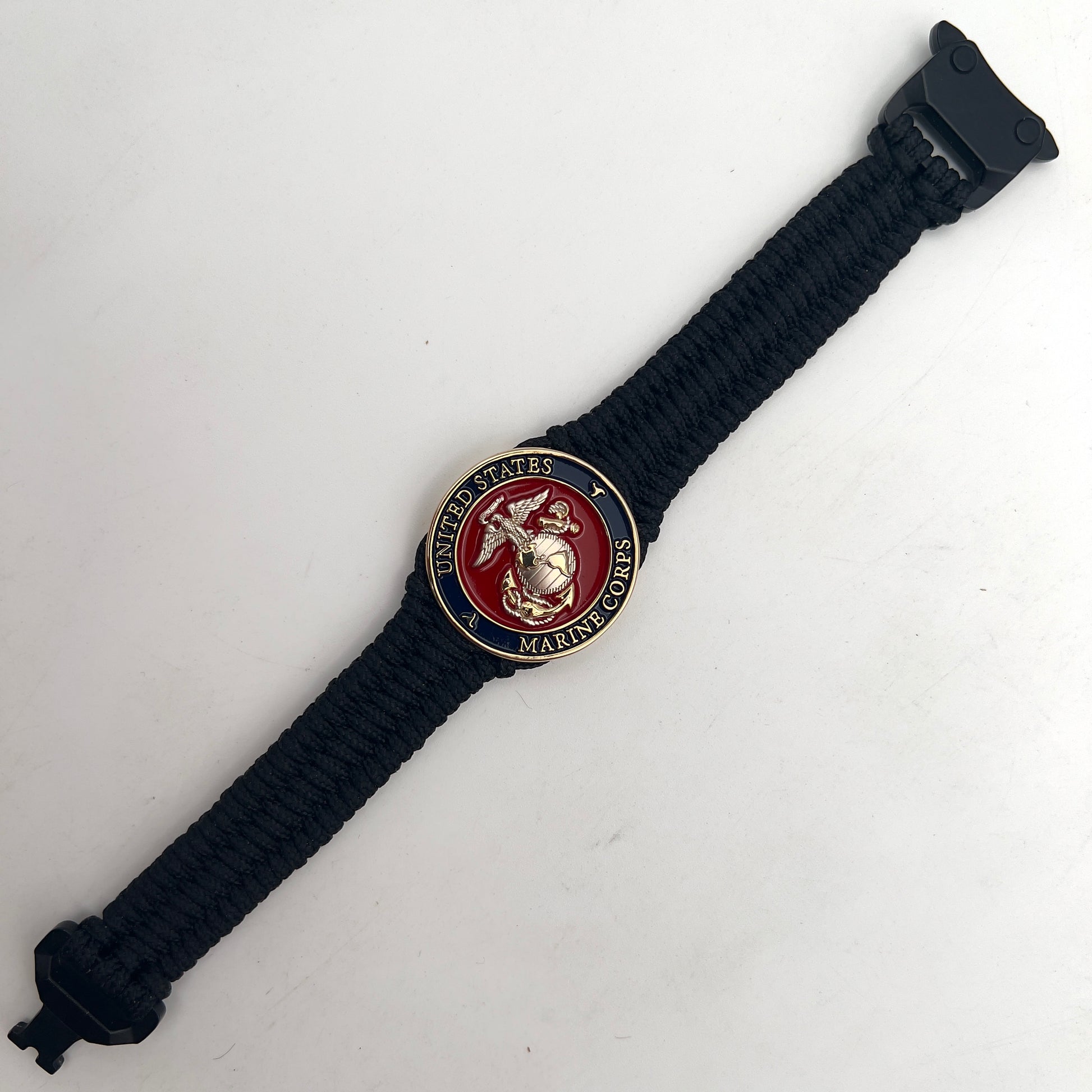 Thin, narrow, flexible and comfortable braided United States Marine Corps bracelet featuring a 24K gold and silver plated USMC Eagle Globe and Anchor medallion, a black Cobra style tactical buckle and woven with black type-1 paracord.
