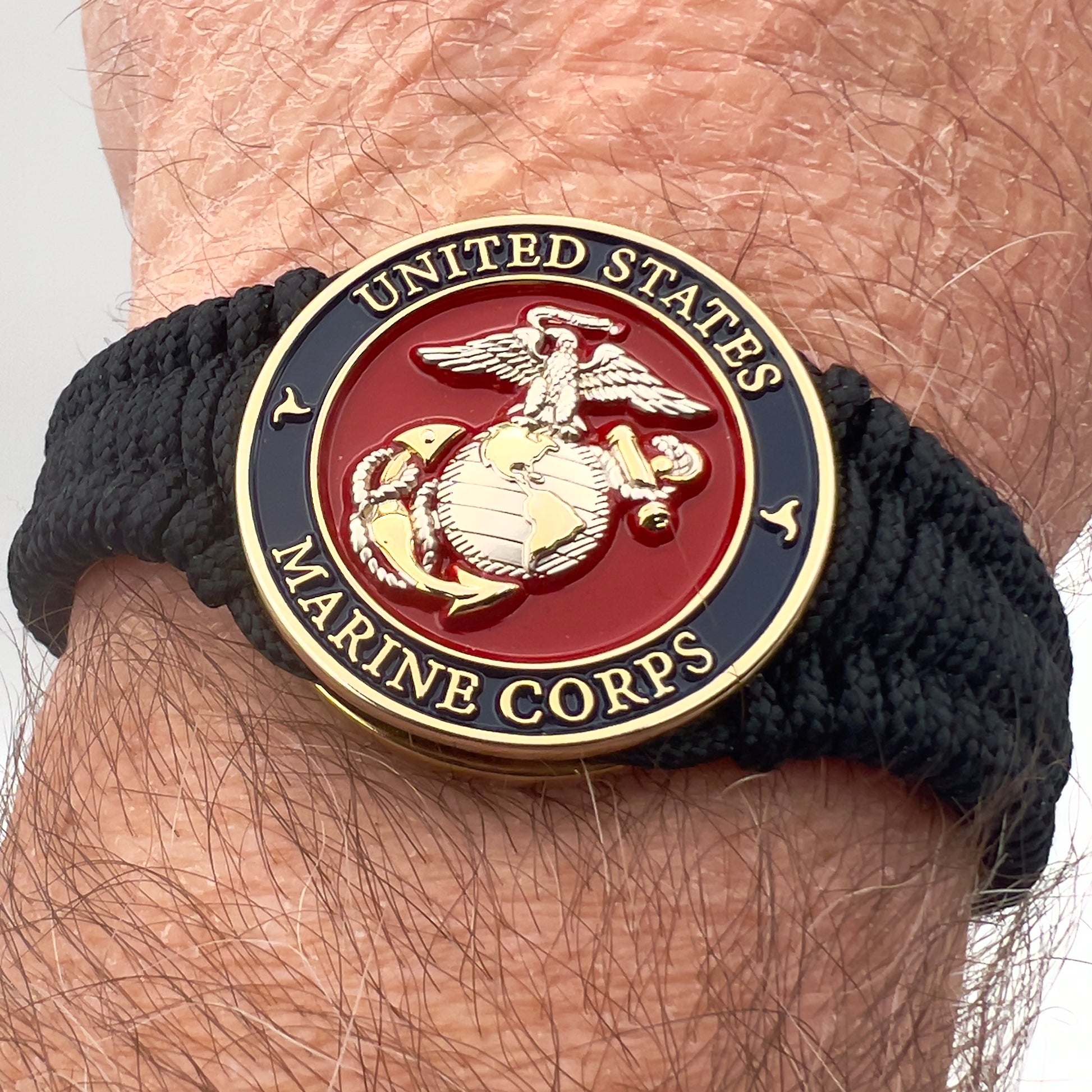 Thin, narrow, flexible and comfortable braided United States Marine Corps bracelet featuring a 24K gold and silver plated USMC Eagle Globe and Anchor medallion, a black Cobra style tactical buckle and woven with black type-1 paracord.