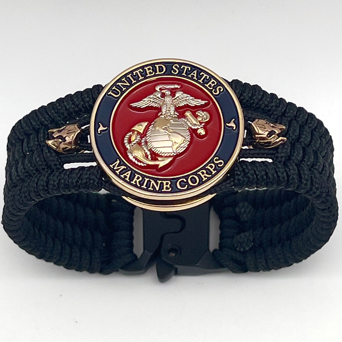 Thin, medium width, flexible and comfortable braided United States Marine Corps bracelet featuring a 24K gold and silver plated USMC officer Eagle Globe and Anchor medallion, two brass micro Spartan helmets, a black Cobra style tactical buckle and woven with black type-1 paracord.