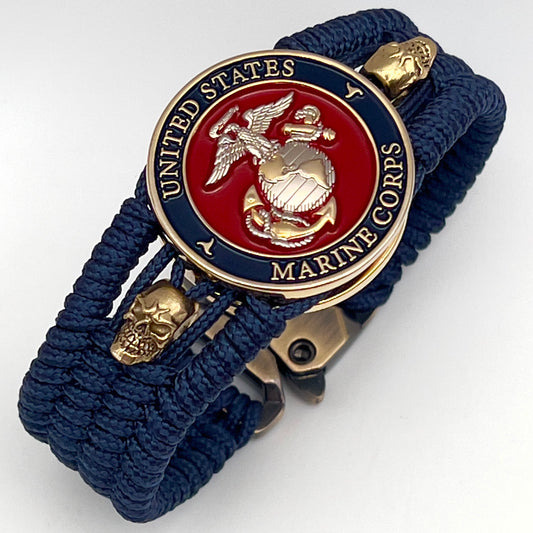 Thin, medium width, flexible and comfortable braided United States Marine Corps bracelet featuring a 24K gold and silver plated USMC officer Eagle Globe and Anchor medallion, two gold micro skulls, a gold Cobra style tactical buckle and woven with Navy blue type-1 paracord.