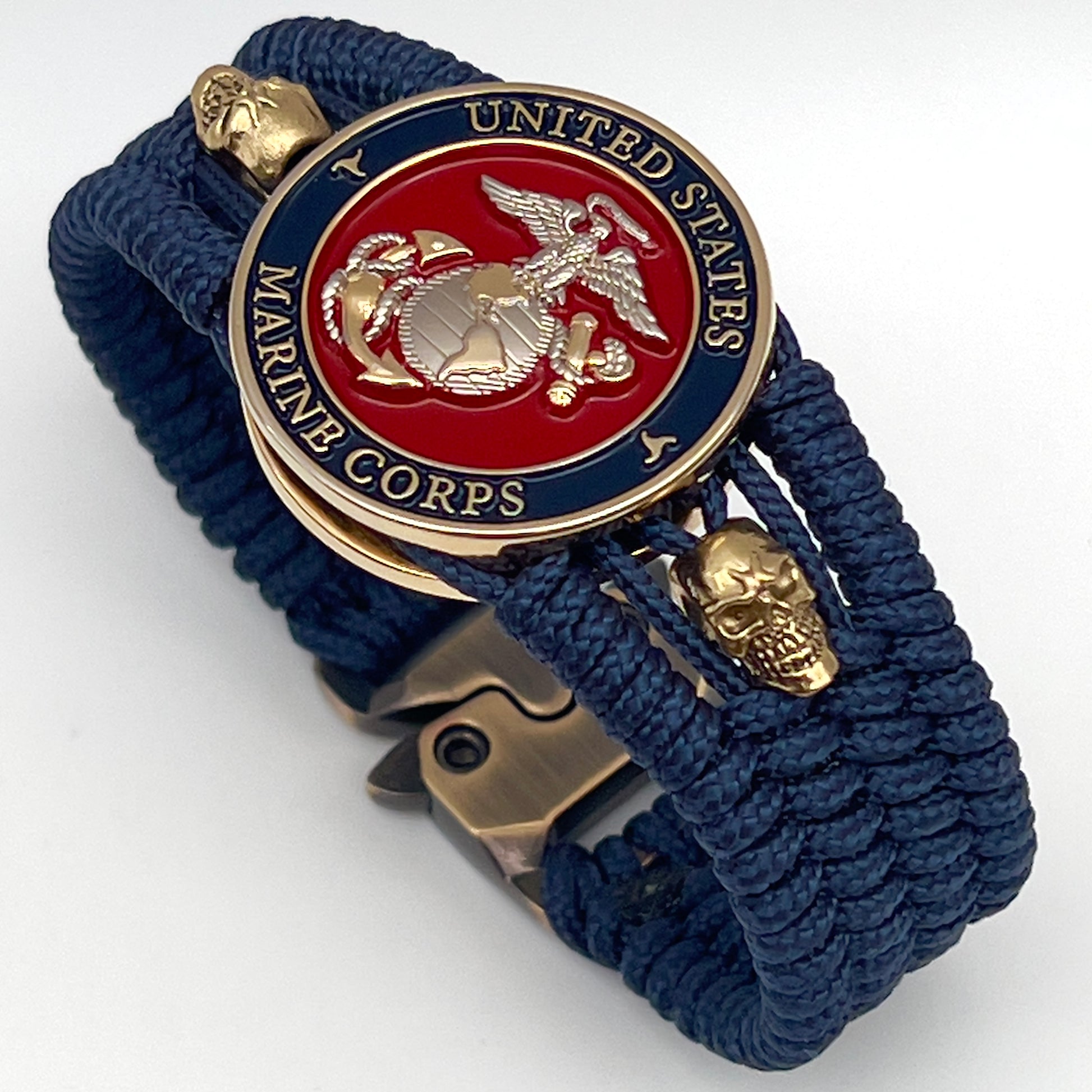 Thin, medium width, flexible and comfortable braided United States Marine Corps bracelet featuring a 24K gold and silver plated USMC officer Eagle Globe and Anchor medallion, two gold micro skulls, a gold Cobra style tactical buckle and woven with Navy blue type-1 paracord.