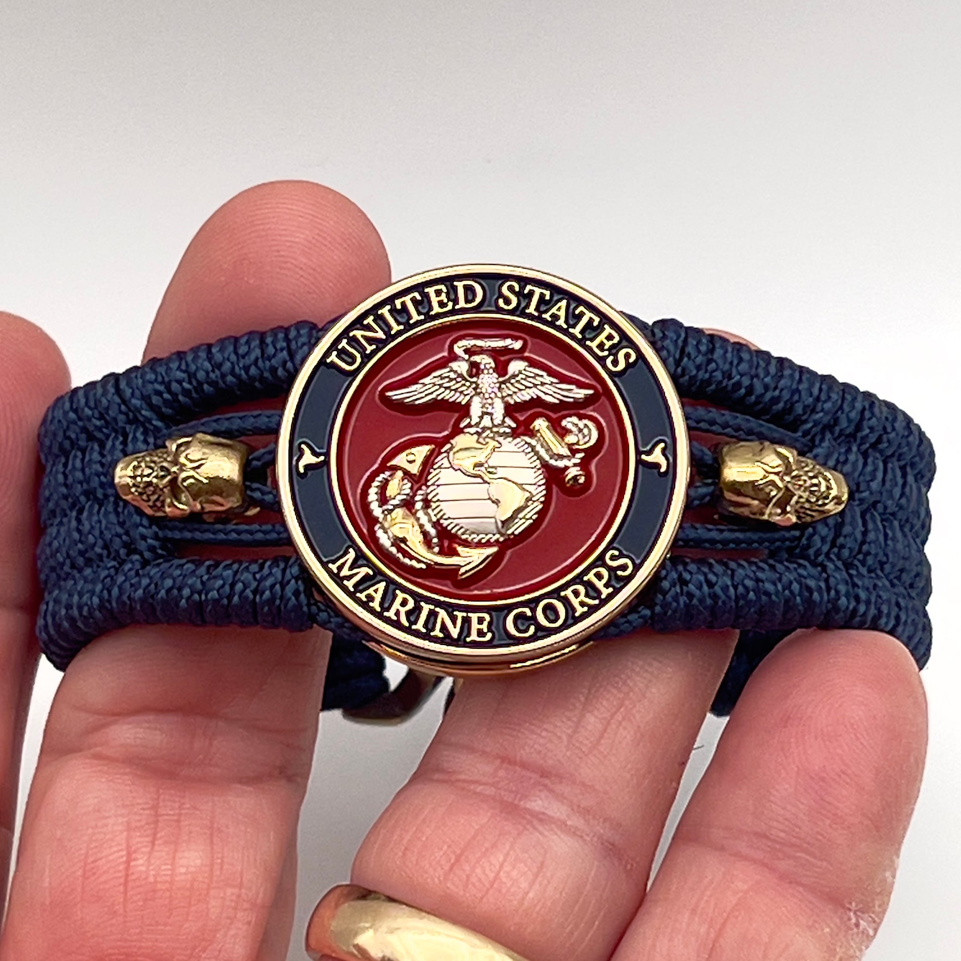 Thin, medium width, flexible and comfortable braided United States Marine Corps bracelet featuring a 24K gold and silver plated USMC officer Eagle Globe and Anchor medallion, two gold micro skulls, a gold Cobra style tactical buckle and woven with Navy blue type-1 paracord.
