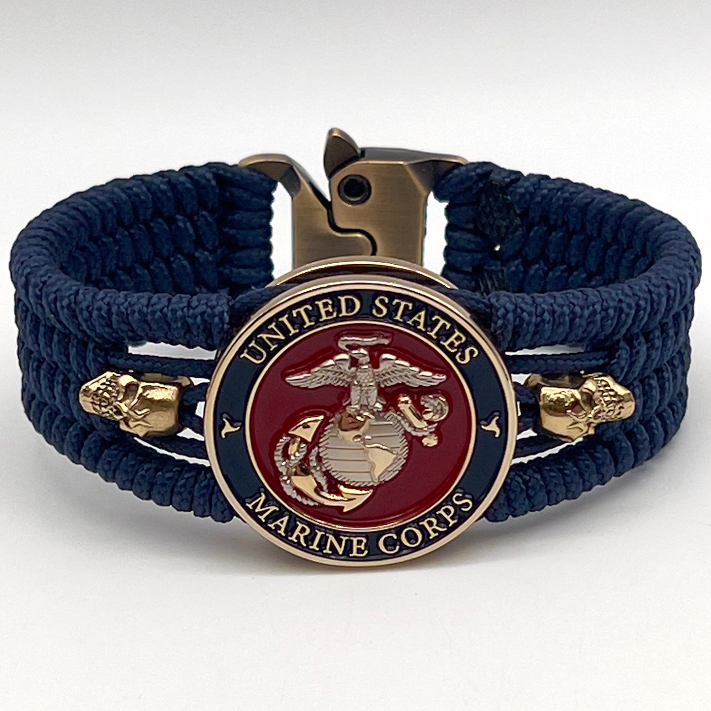 Thin, medium width, flexible and comfortable braided United States Marine Corps bracelet featuring a 24K gold and silver plated USMC officer Eagle Globe and Anchor medallion, two gold micro skulls, a gold Cobra style tactical buckle and woven with Navy blue type-1 paracord.