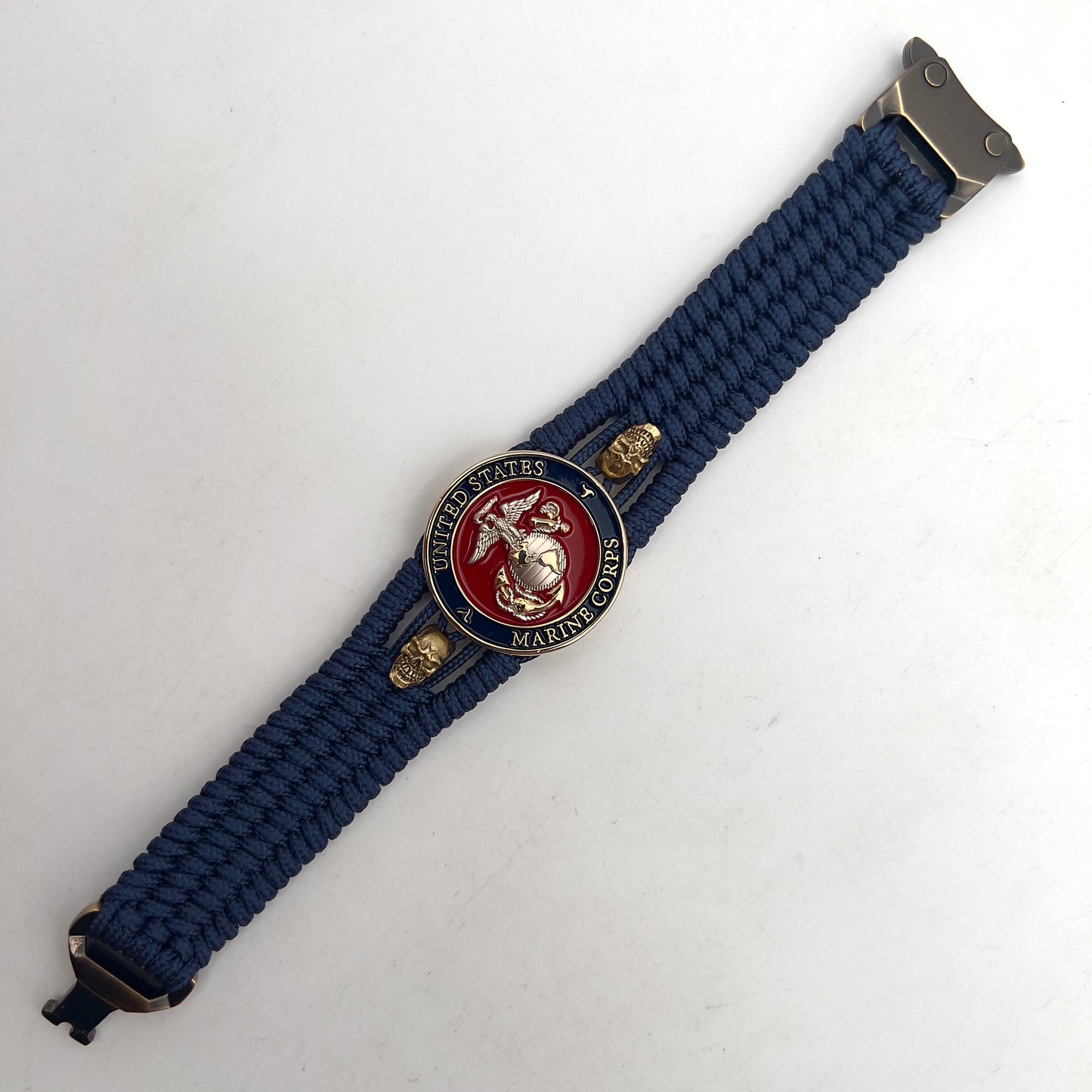 Thin, medium width, flexible and comfortable braided United States Marine Corps bracelet featuring a 24K gold and silver plated USMC officer Eagle Globe and Anchor medallion, two gold micro skulls, a gold Cobra style tactical buckle and woven with Navy blue type-1 paracord.