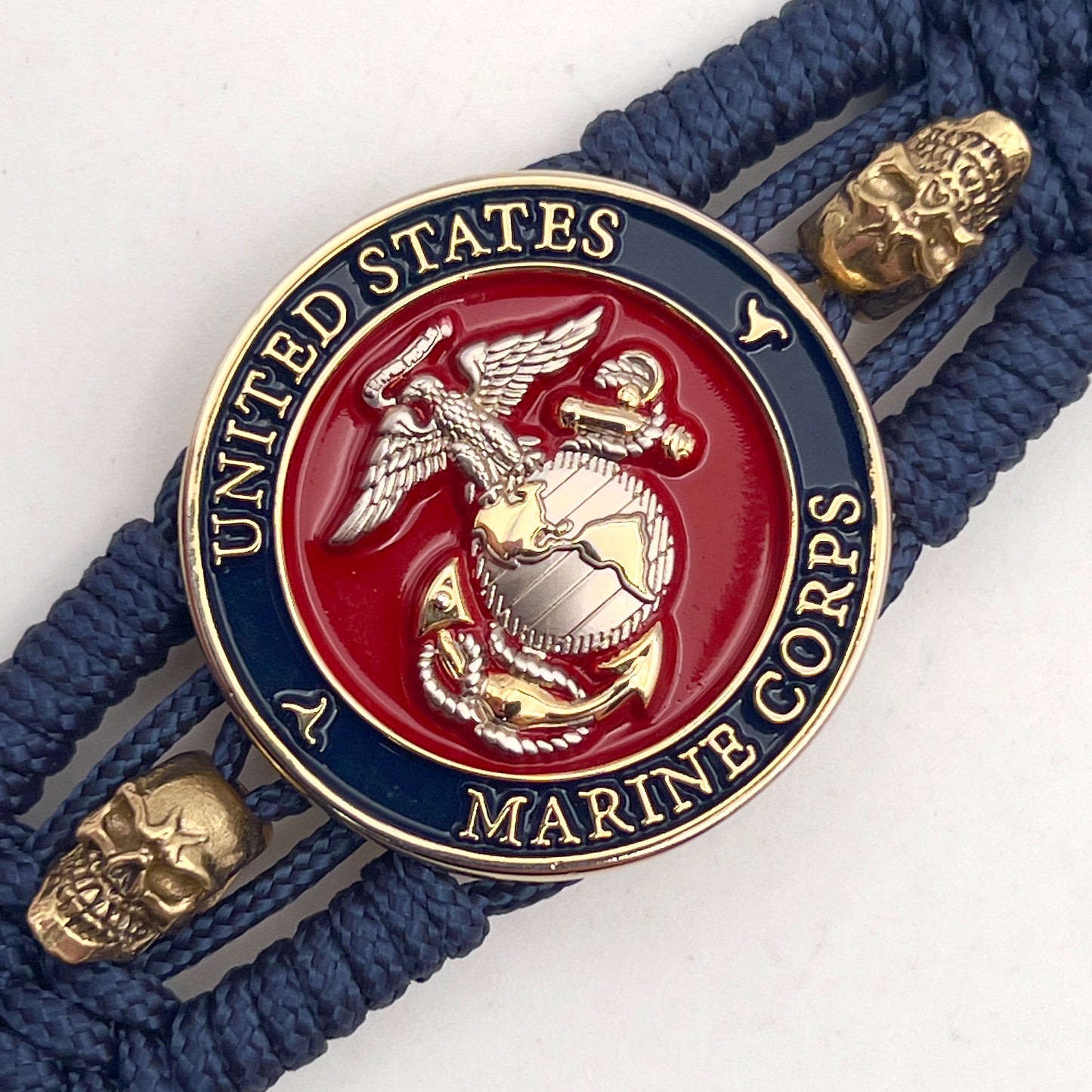 Thin, medium width, flexible and comfortable braided United States Marine Corps bracelet featuring a 24K gold and silver plated USMC officer Eagle Globe and Anchor medallion, two gold micro skulls, a gold Cobra style tactical buckle and woven with Navy blue type-1 paracord.