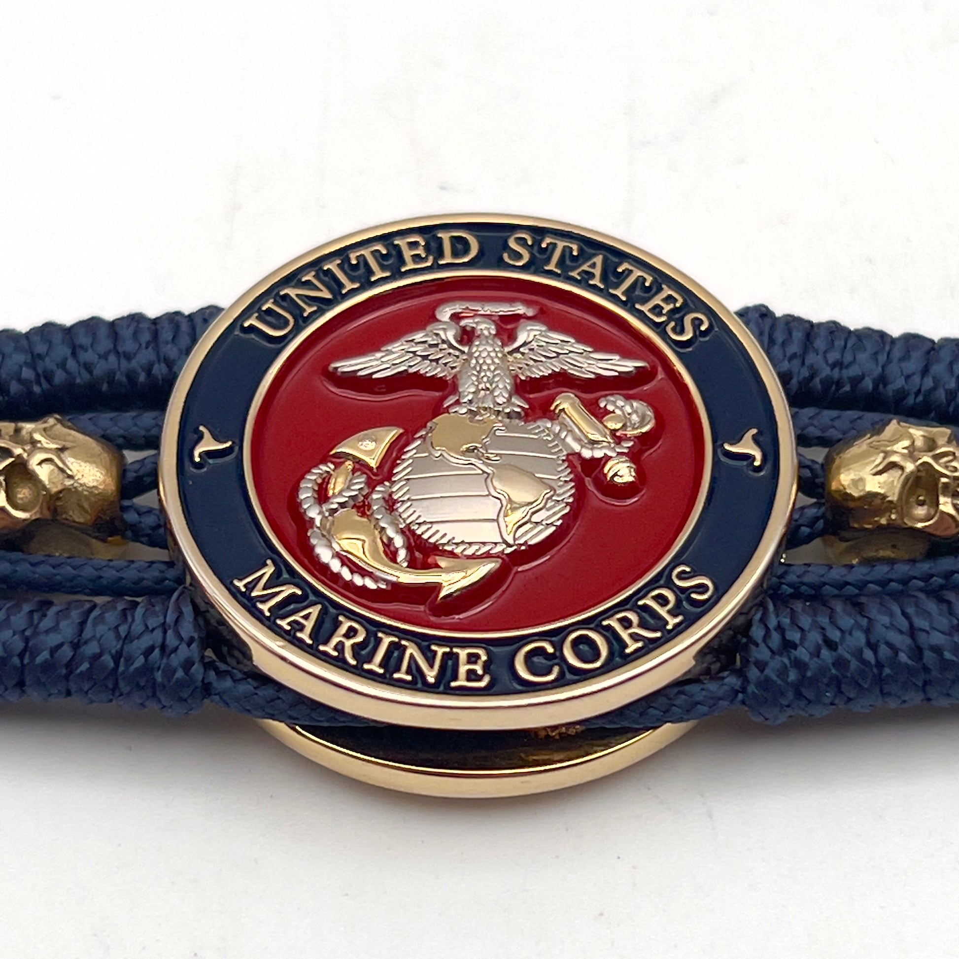 Thin, medium width, flexible and comfortable braided United States Marine Corps bracelet featuring a 24K gold and silver plated USMC officer Eagle Globe and Anchor medallion, two gold micro skulls, a gold Cobra style tactical buckle and woven with Navy blue type-1 paracord.