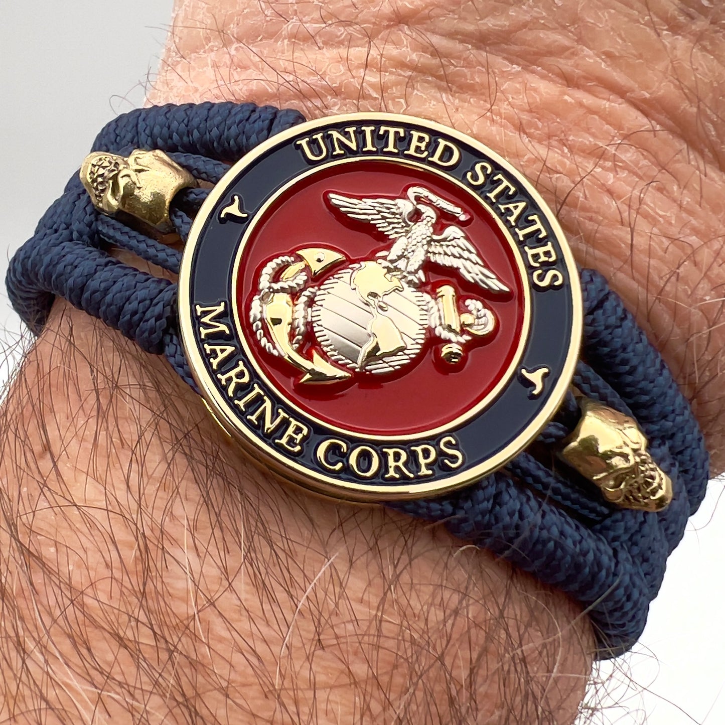 Thin, medium width, flexible and comfortable braided United States Marine Corps bracelet featuring a 24K gold and silver plated USMC officer Eagle Globe and Anchor medallion, two gold micro skulls, a gold Cobra style tactical buckle and woven with Navy blue type-1 paracord.