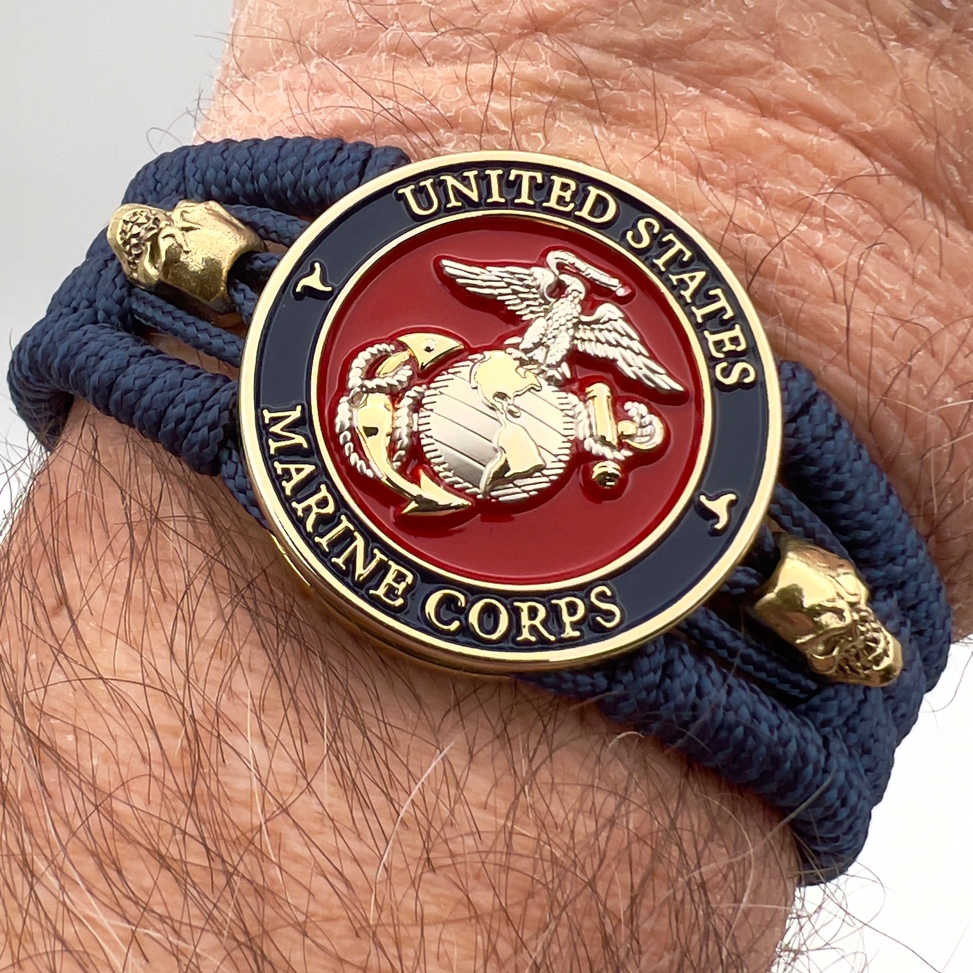 Thin, medium width, flexible and comfortable braided United States Marine Corps bracelet featuring a 24K gold and silver plated USMC officer Eagle Globe and Anchor medallion, two gold micro skulls, a gold Cobra style tactical buckle and woven with Navy blue type-1 paracord.