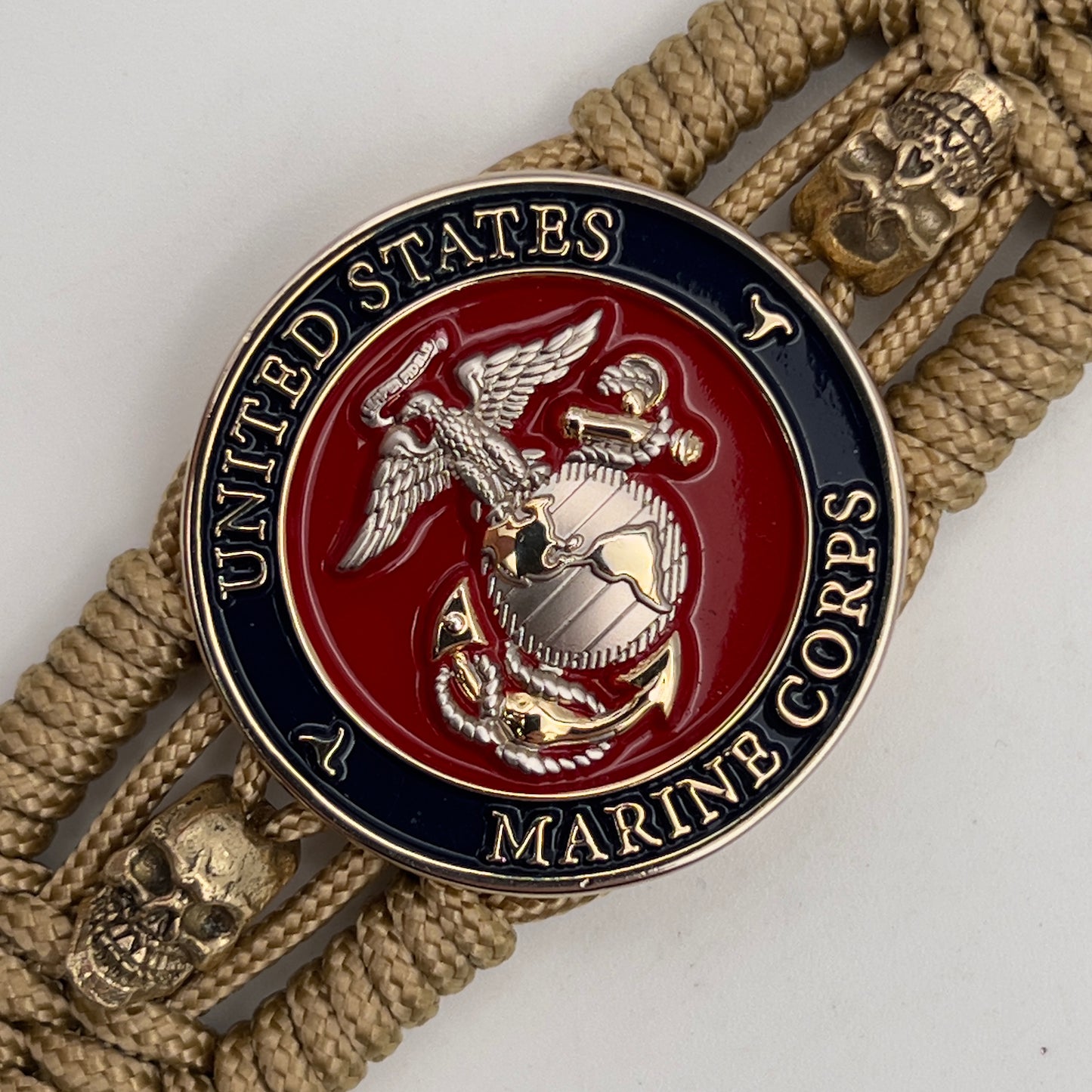 Thin, medium width, flexible and comfortable braided United States Marine Corps bracelet featuring a 24K gold and silver plated USMC officer Eagle Globe and Anchor medallion, two gold micro skulls, a gold Cobra style tactical buckle and woven with gold type-1 paracord.
