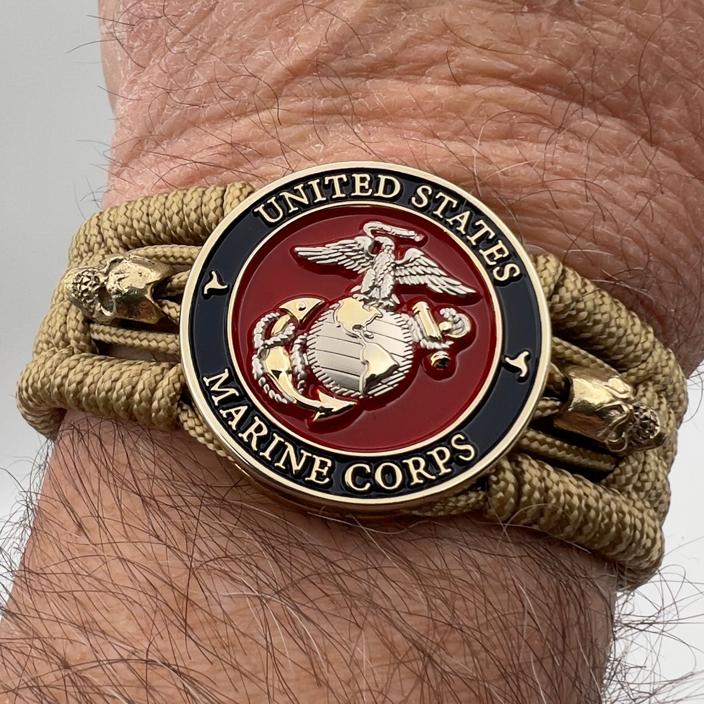 Thin, medium width, flexible and comfortable braided United States Marine Corps bracelet featuring a 24K gold and silver plated USMC officer Eagle Globe and Anchor medallion, two gold micro skulls, a gold Cobra style tactical buckle and woven with gold type-1 paracord.