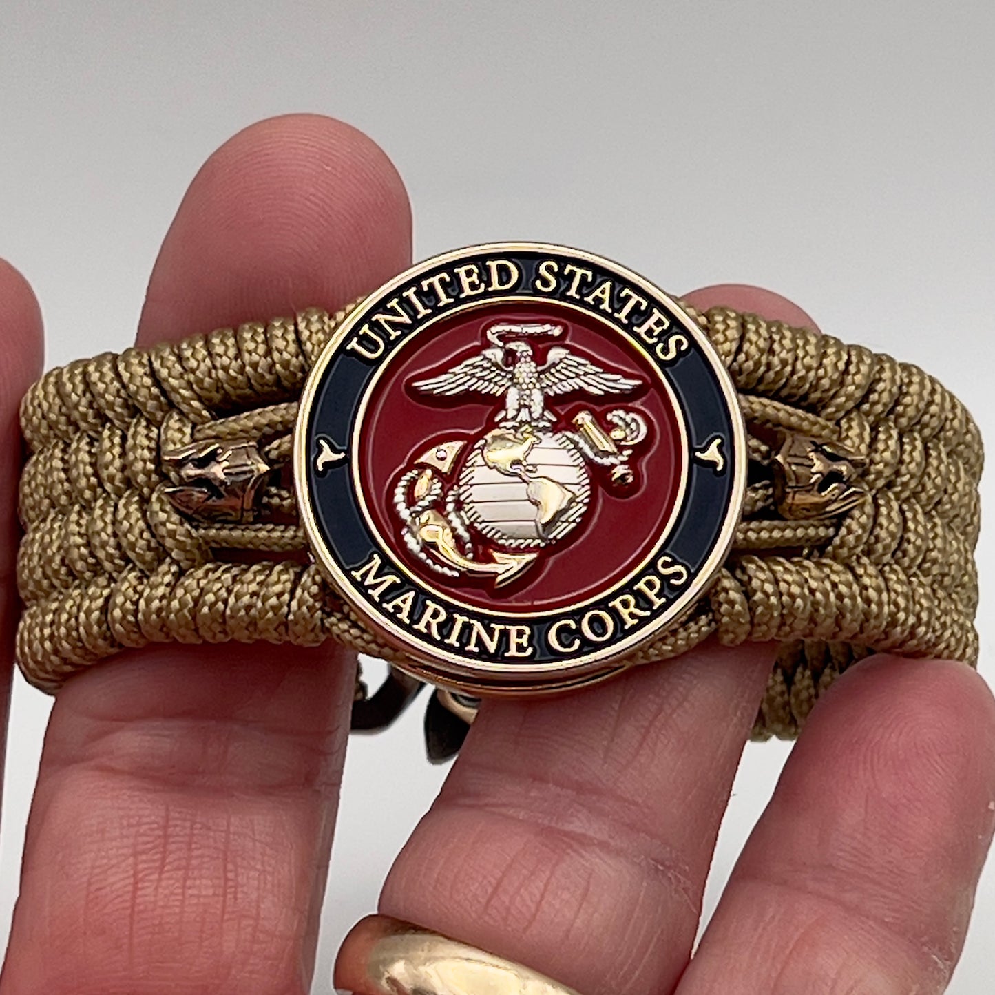 Thin, medium width, flexible and comfortable braided United States Marine Corps bracelet featuring a 24K gold and silver plated USMC officer Eagle Globe and Anchor medallion, two brass micro Spartan helmets, a gold Cobra style tactical buckle and woven with gold type-1 paracord.