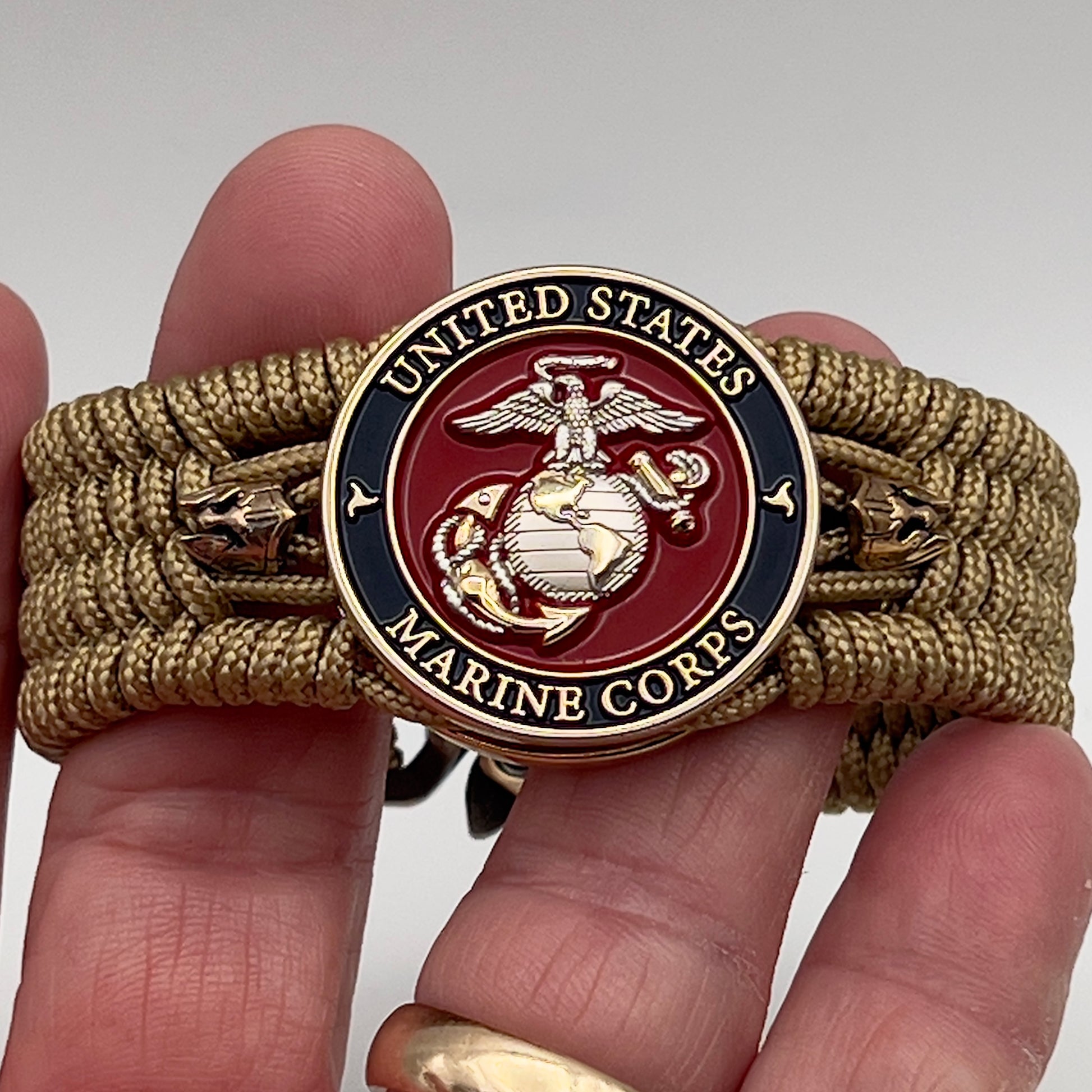 Thin, medium width, flexible and comfortable braided United States Marine Corps bracelet featuring a 24K gold and silver plated USMC officer Eagle Globe and Anchor medallion, two brass micro Spartan helmets, a gold Cobra style tactical buckle and woven with gold type-1 paracord.