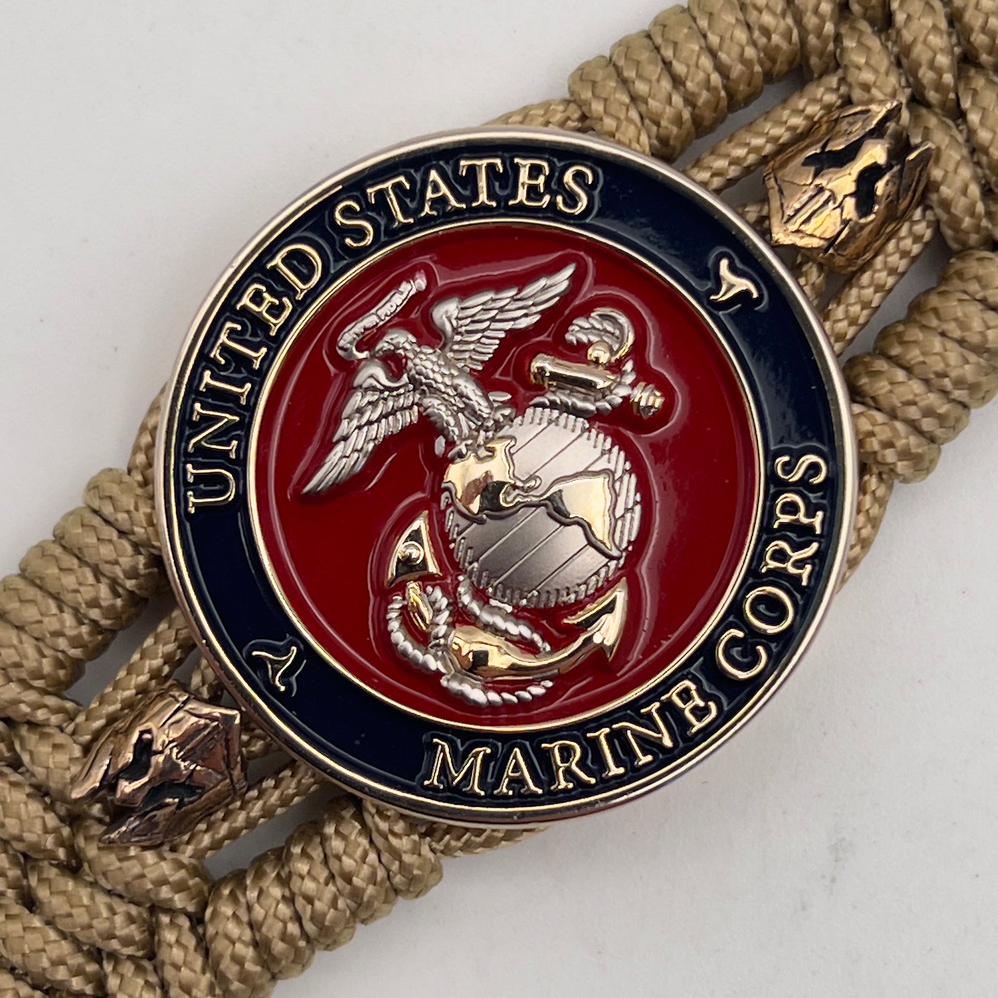 Thin, medium width, flexible and comfortable braided United States Marine Corps bracelet featuring a 24K gold and silver plated USMC officer Eagle Globe and Anchor medallion, two brass micro Spartan helmets, a gold Cobra style tactical buckle and woven with gold type-1 paracord.