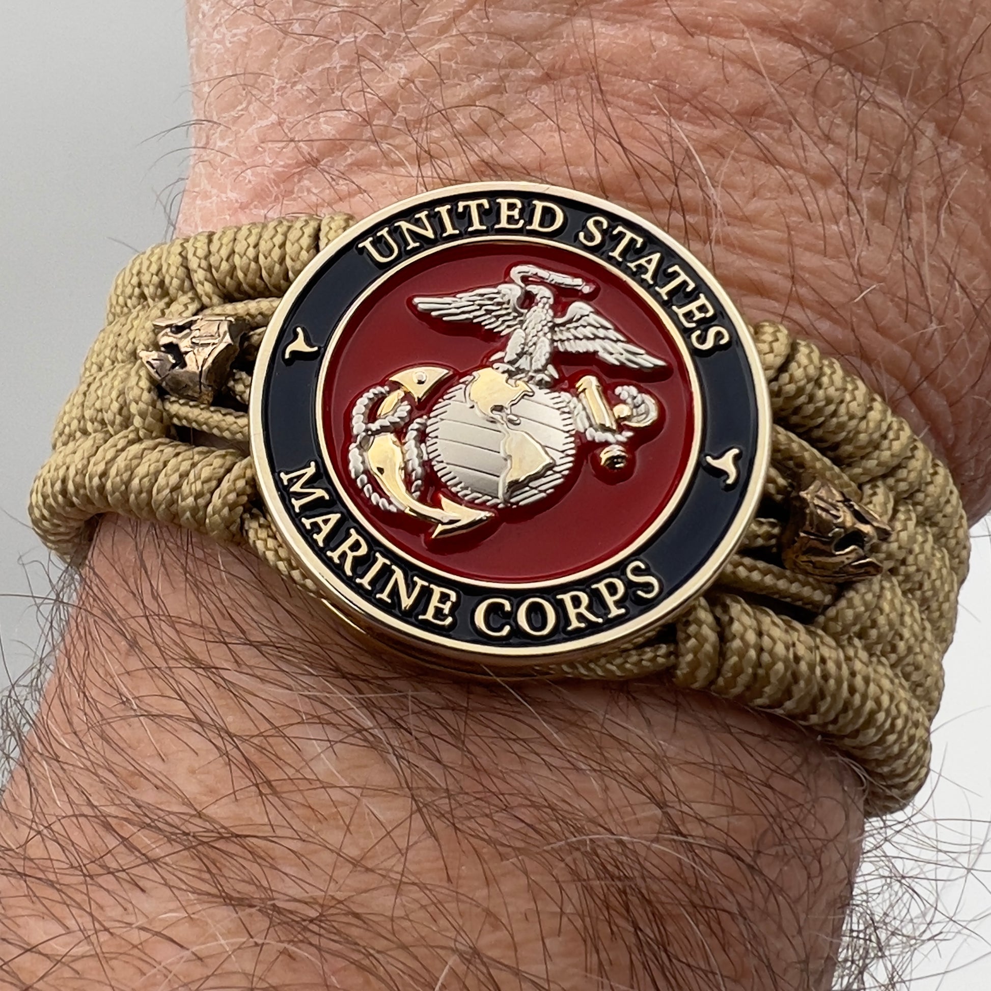 Thin, medium width, flexible and comfortable braided United States Marine Corps bracelet featuring a 24K gold and silver plated USMC officer Eagle Globe and Anchor medallion, two brass micro Spartan helmets, a gold Cobra style tactical buckle and woven with gold type-1 paracord.